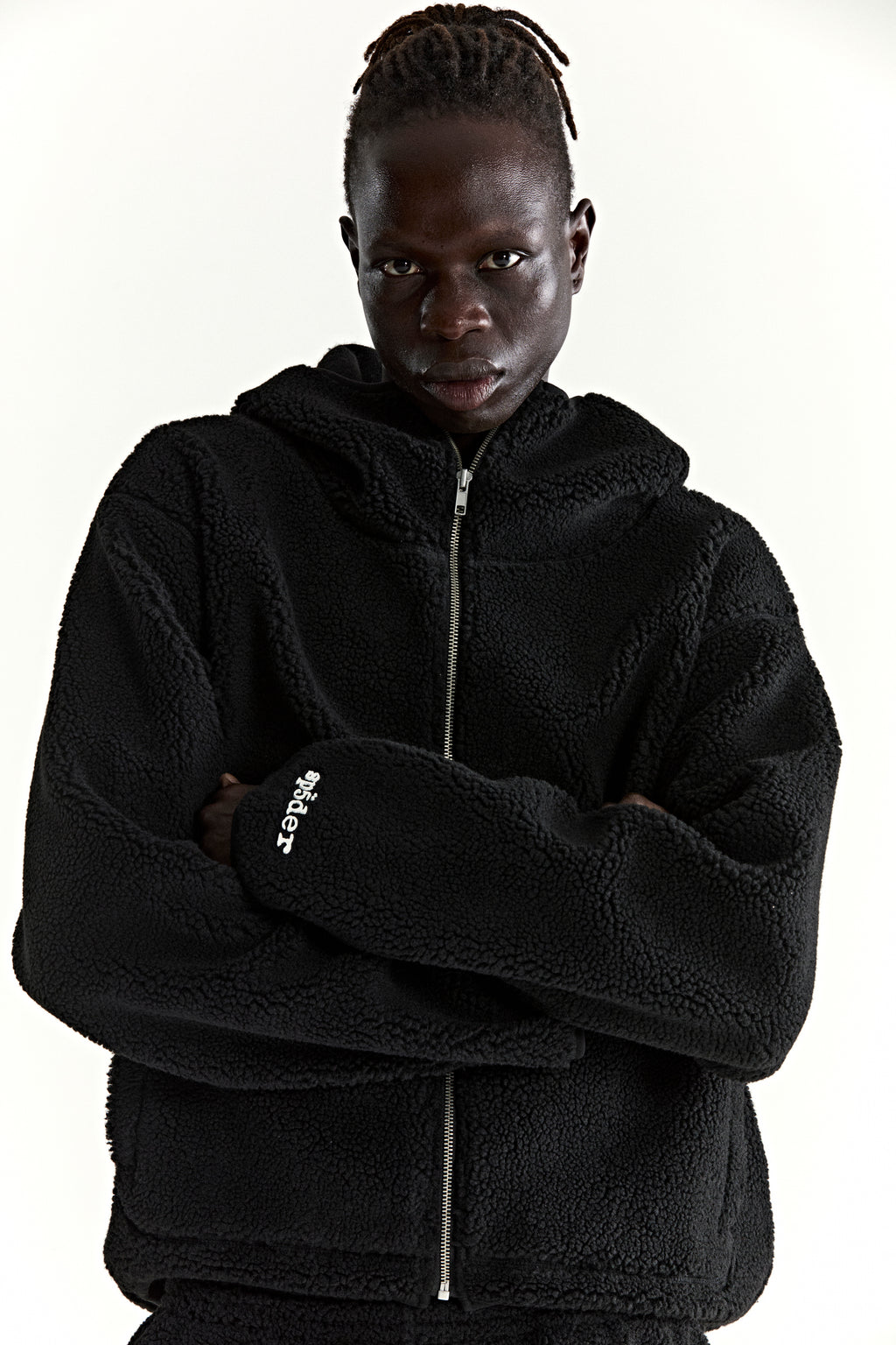 Black teddy fleece zip-up hooded jacket with a rubberized logo patch on the wrist.