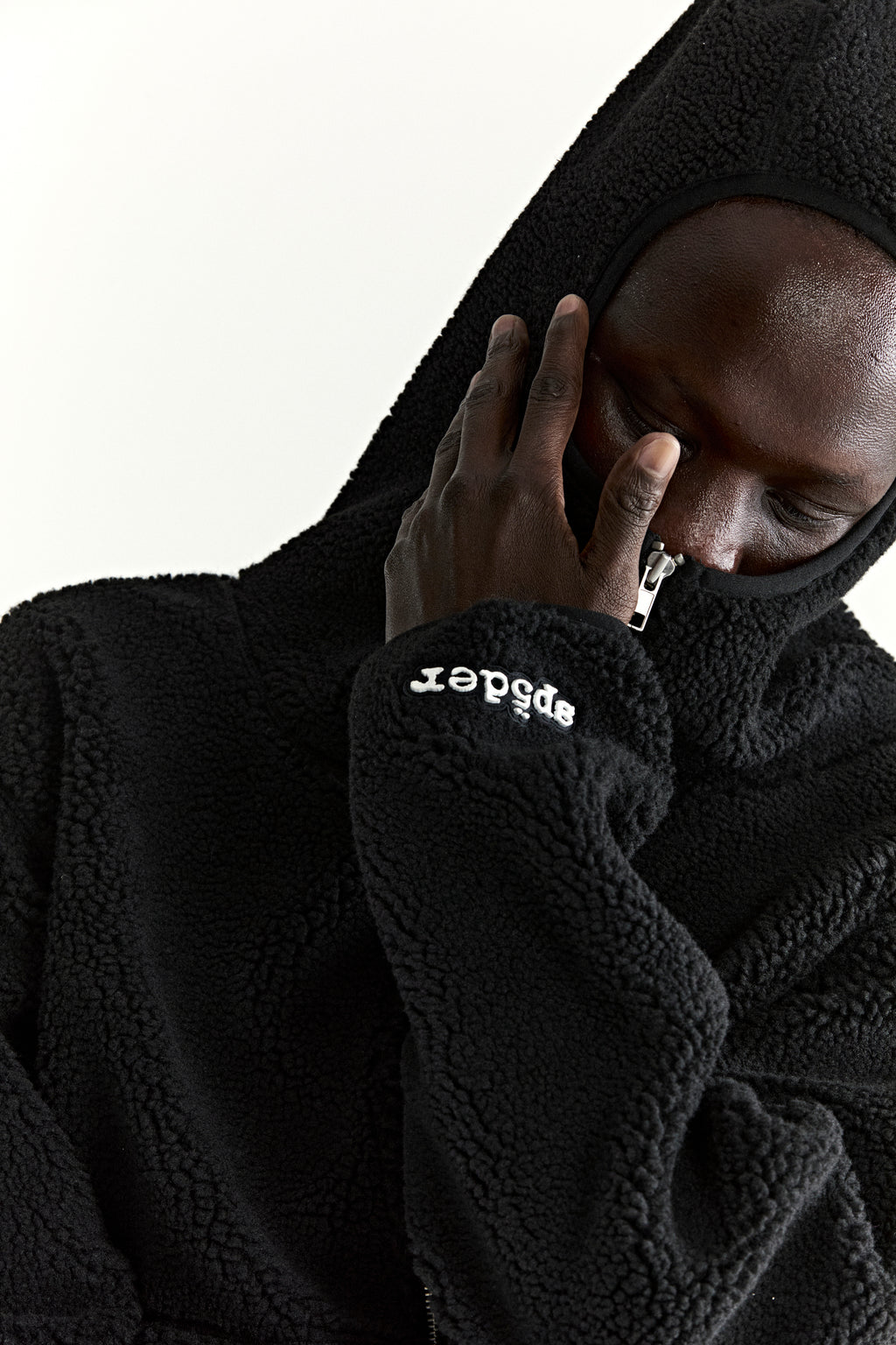 Black teddy fleece zip-up jacket with hood, rubberized logo patch on wrist, and welt pockets.
