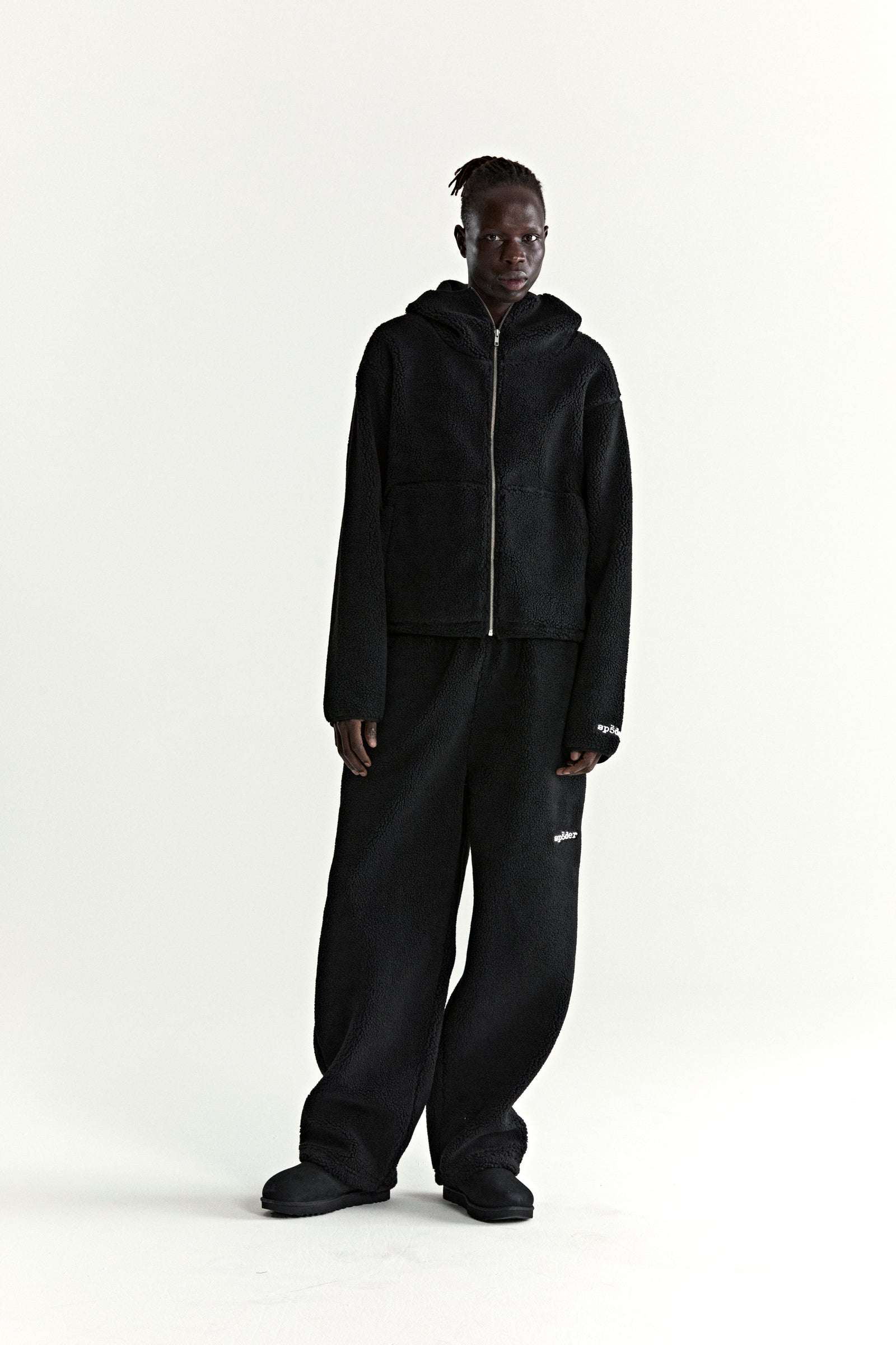 Black teddy fleece zip-up hoodie with rubberized logo patch on wrist, paired with matching fleece pants.