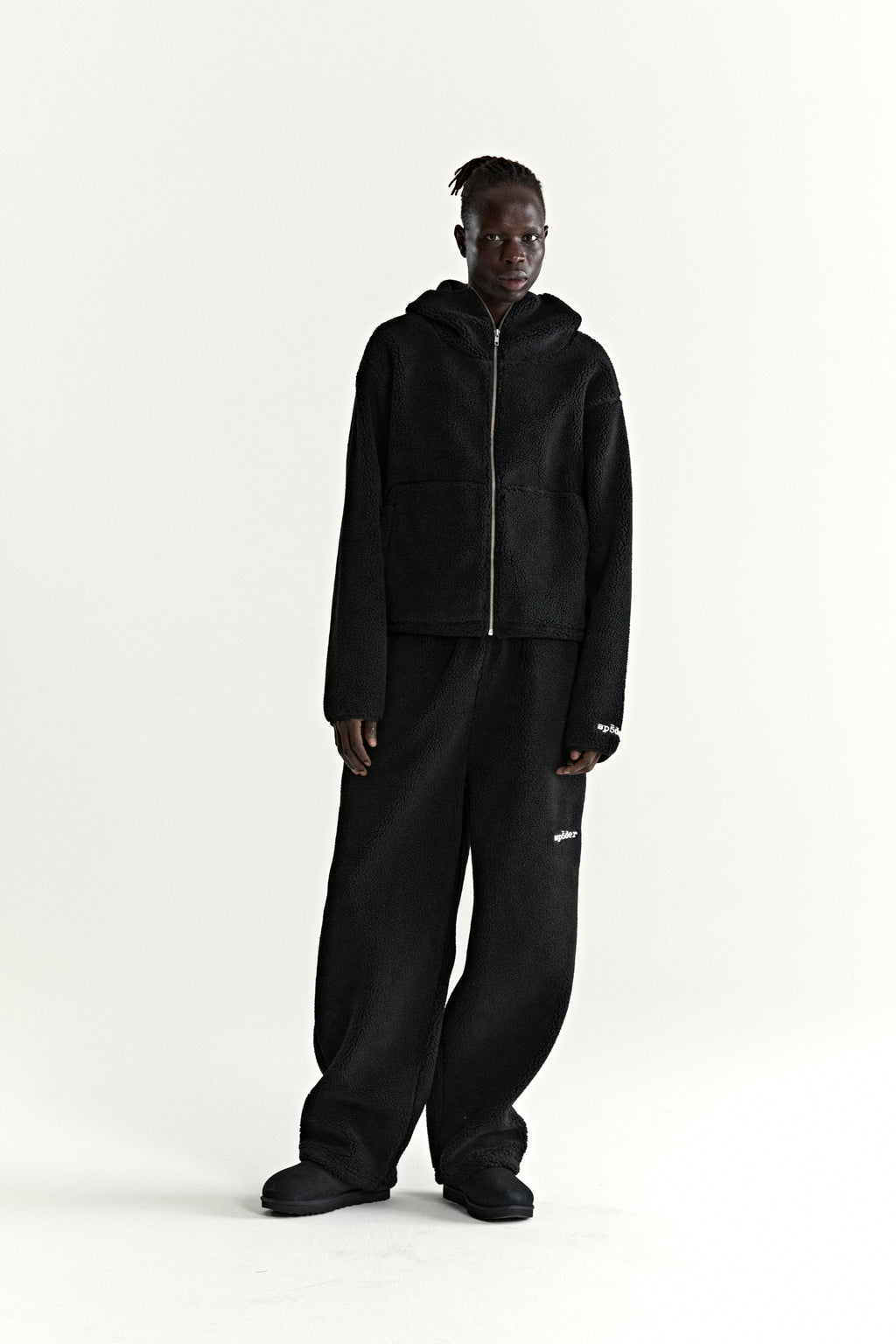 Black teddy fleece zip-up hoodie with rubberized logo patch on wrist, paired with matching fleece pants.