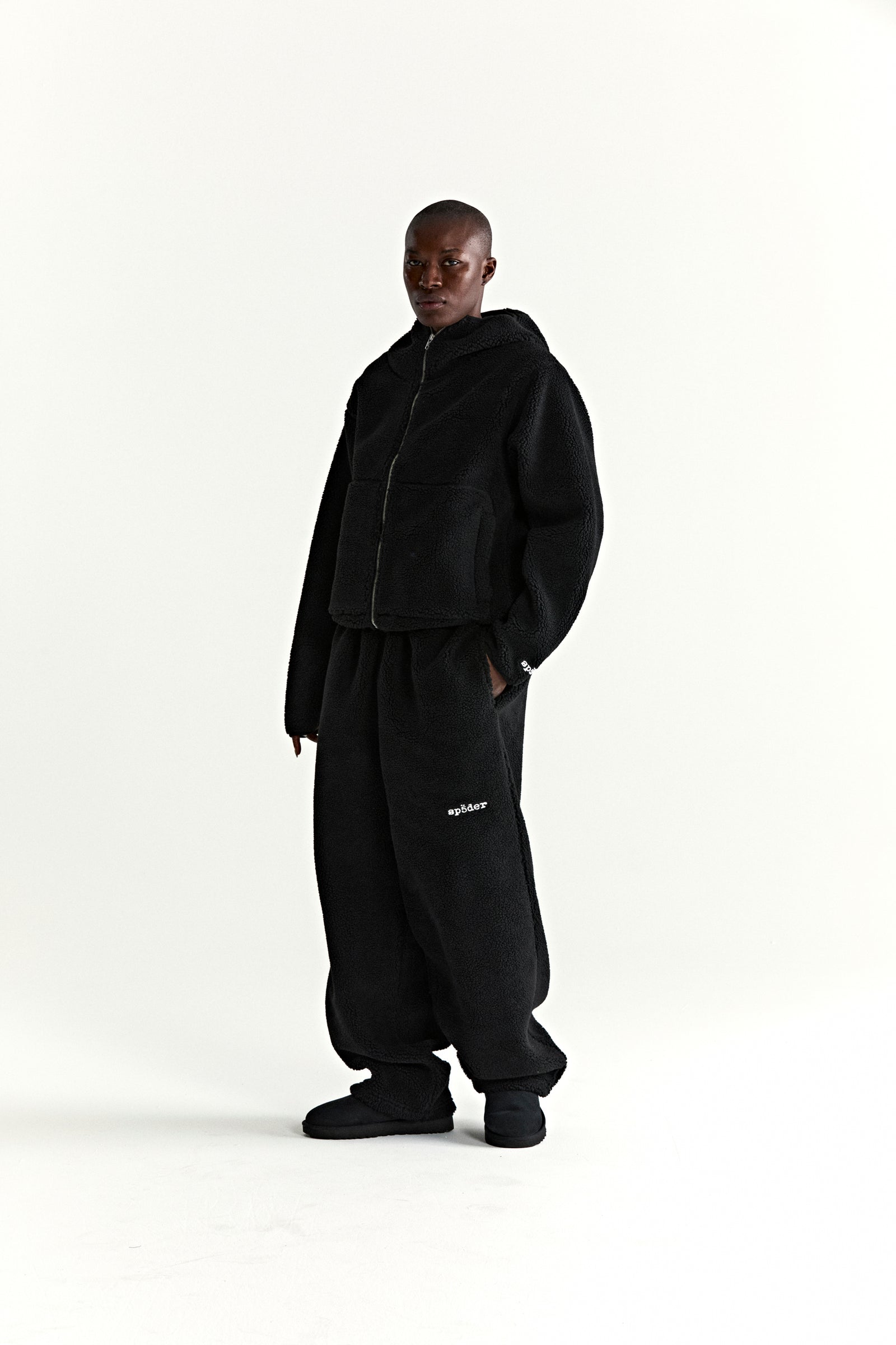 Black teddy fleece zip-up jacket with hood and matching sweatpants, featuring a wrist logo patch.