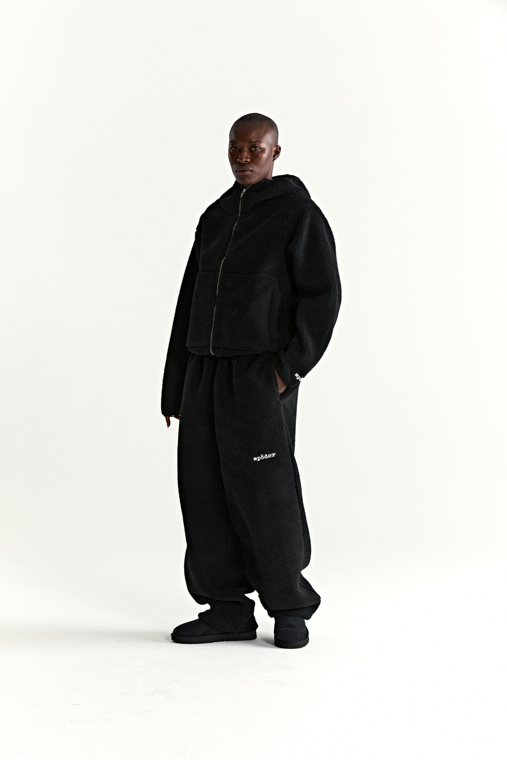 Black teddy fleece zip-up jacket with hood and matching sweatpants, featuring a wrist logo patch.