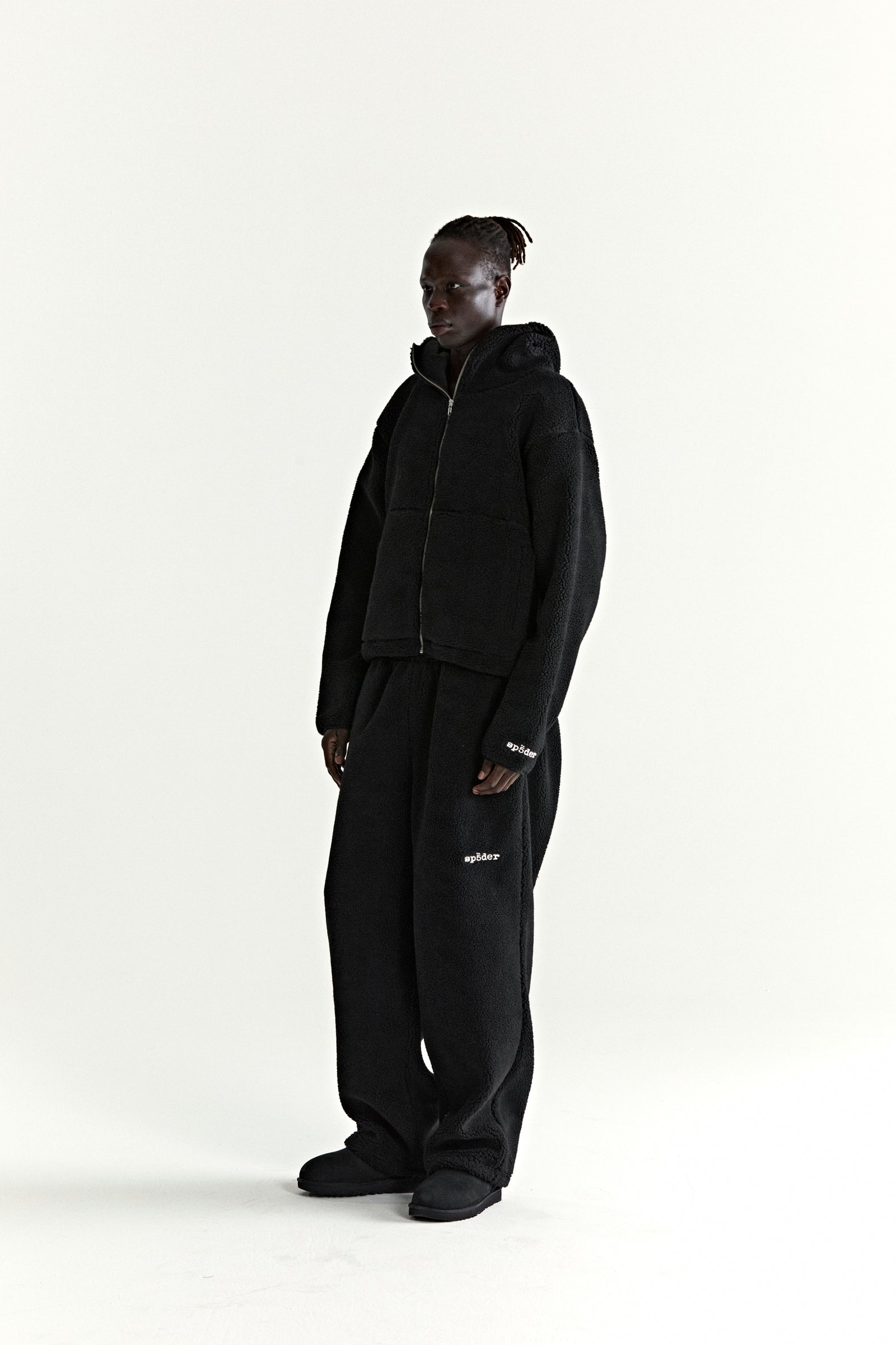 Black teddy fleece zip-up hooded jacket and matching pants with white logo patches.