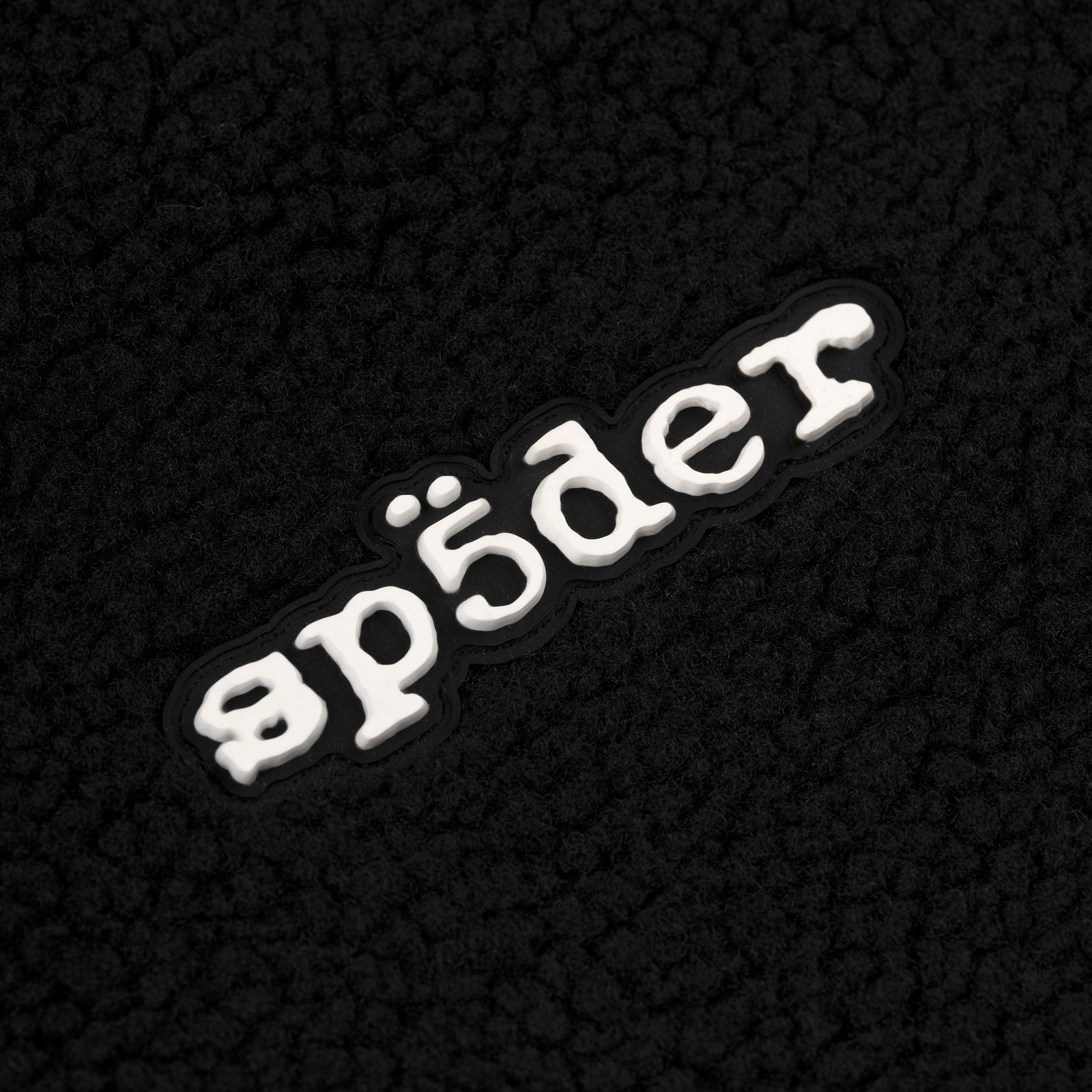 Black teddy fleece zip-up jacket with a white rubberized "sp5der" logo patch on the wrist.