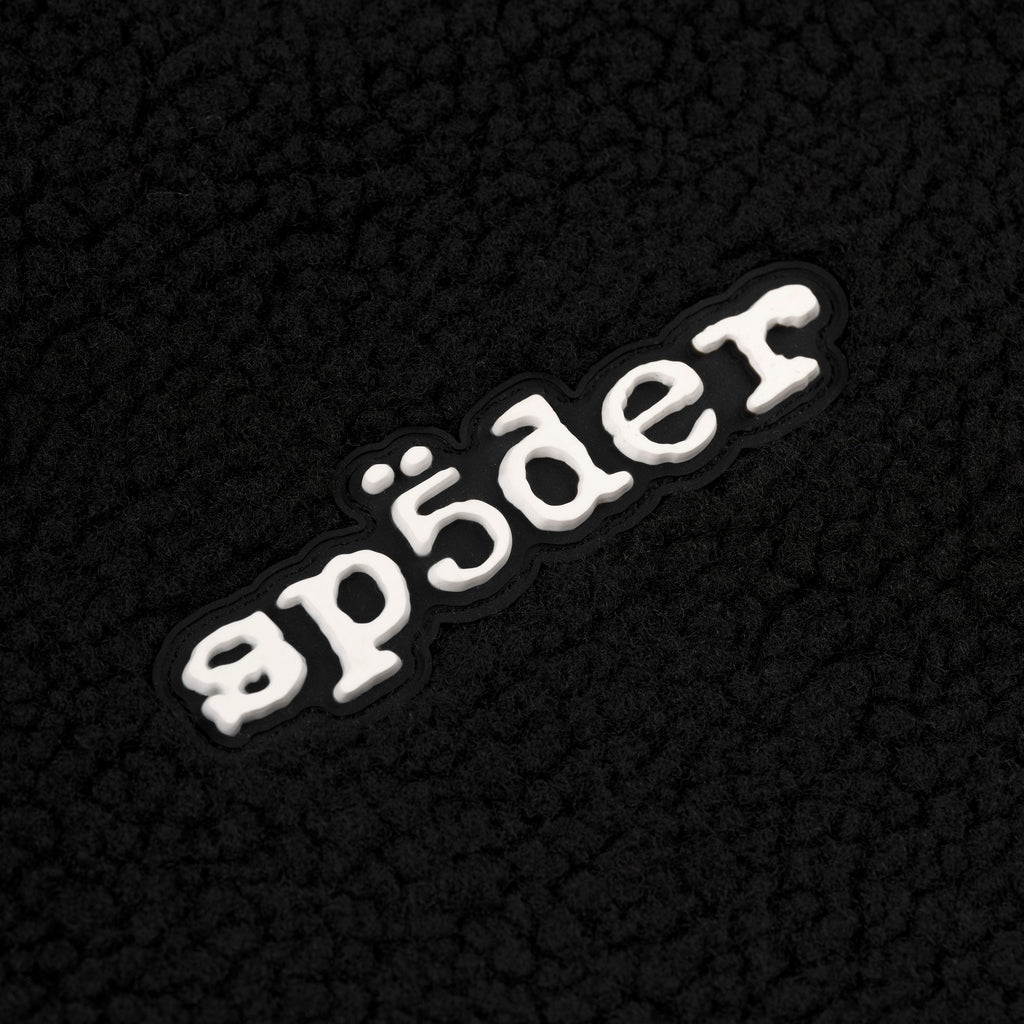 Black teddy fleece zip-up jacket with a white rubberized "sp5der" logo patch on the wrist.