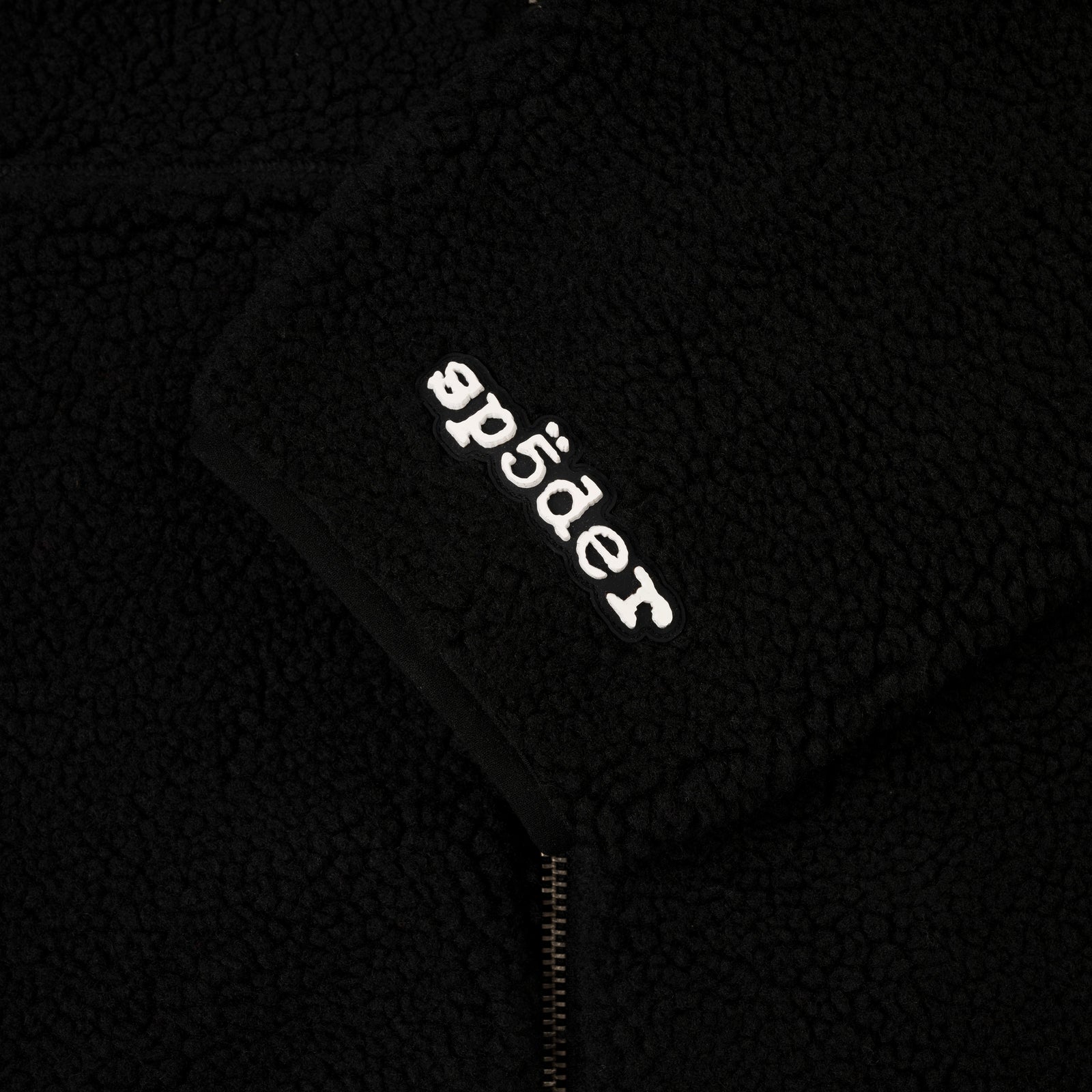 Black teddy fleece zip-up jacket with white "sp5der" logo on the sleeve.