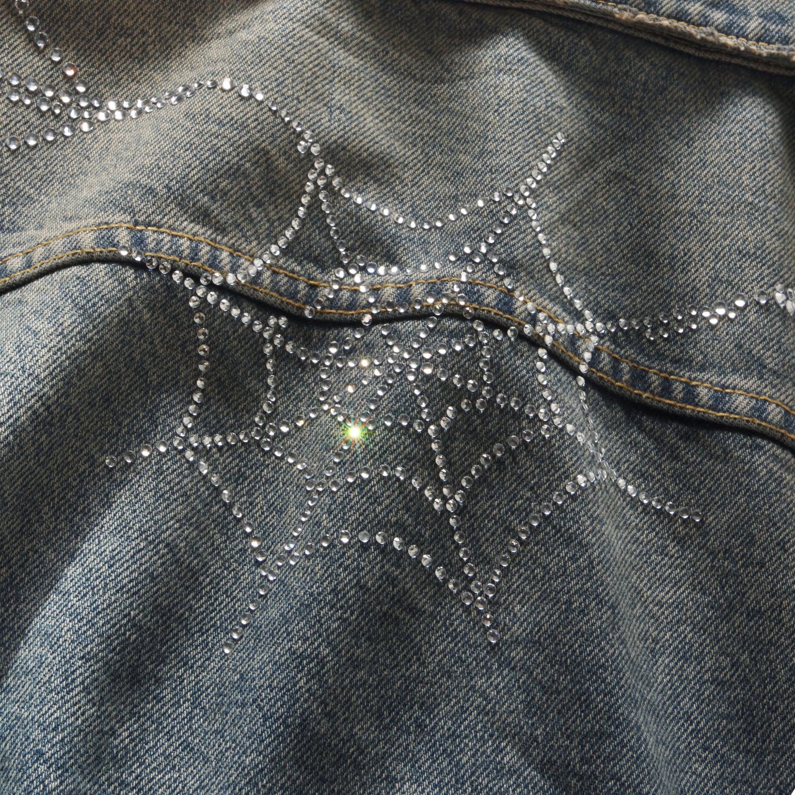 Blue denim jacket featuring a sparkling rhinestone web graphic design.