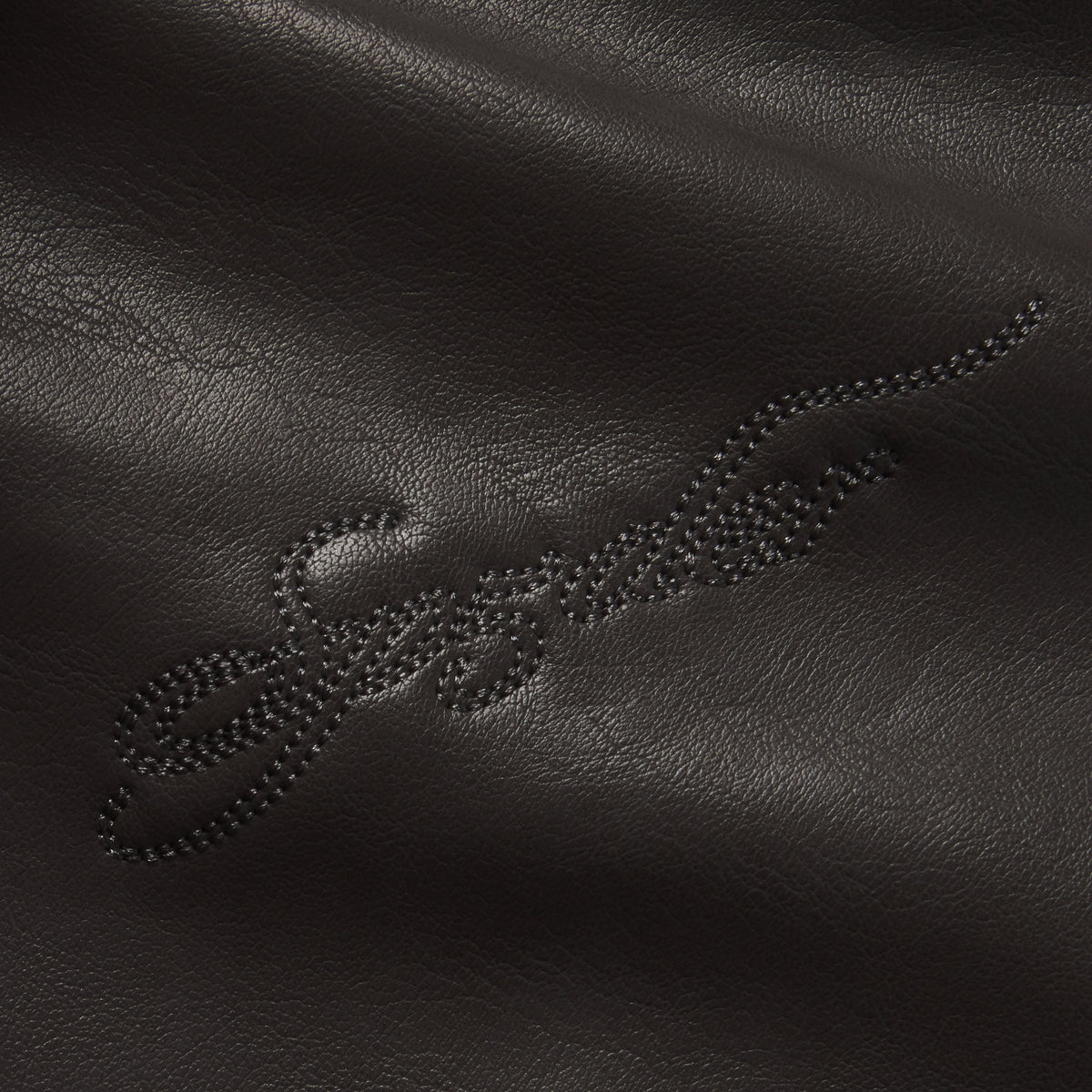 Black faux leather texture featuring tonal SP5DER graphic design embroidery.
