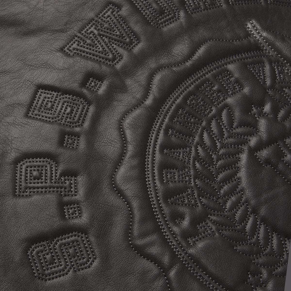 Black faux leather jacket featuring tonal SP5DER graphic design with intricate stitched detailing and embossed branding.