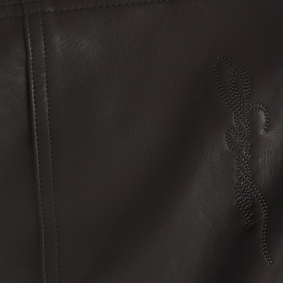 Black faux leather jacket texture featuring subtle tonal SP5DER graphic branding and detailed seam stitching.
