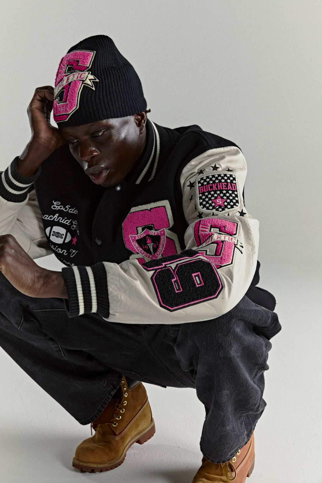 Black wool varsity jacket with cream leather sleeves, pink patches, and striped trim worn by a man.