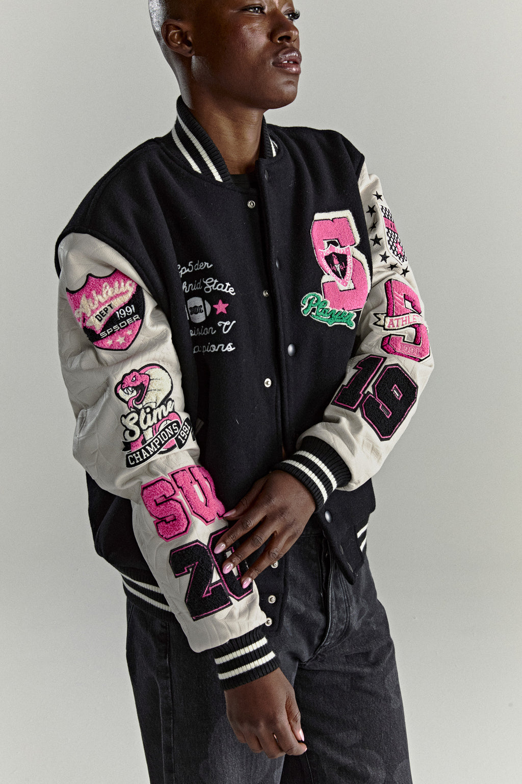 Black wool varsity jacket with cream leather sleeves, pink patches, and striped ribbed trim.