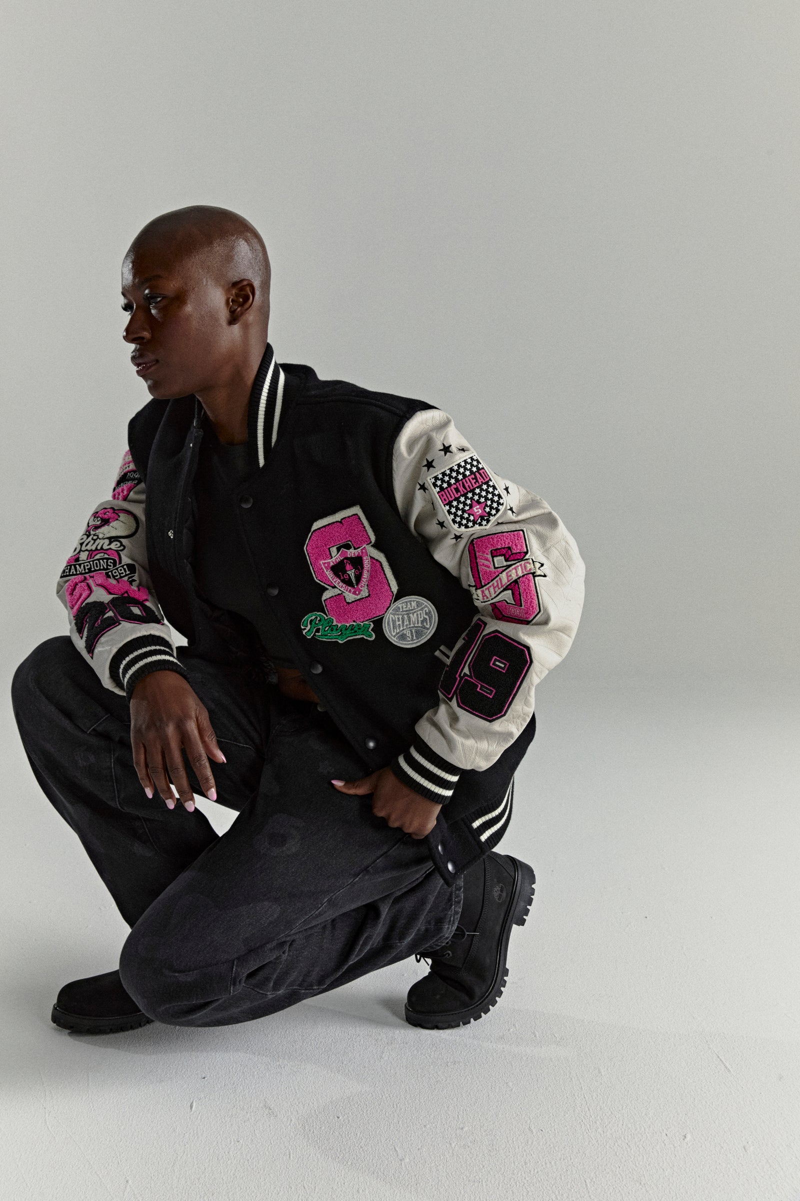 Black wool varsity jacket with contrasting leather sleeves, pink patches, and striped ribbed trim.