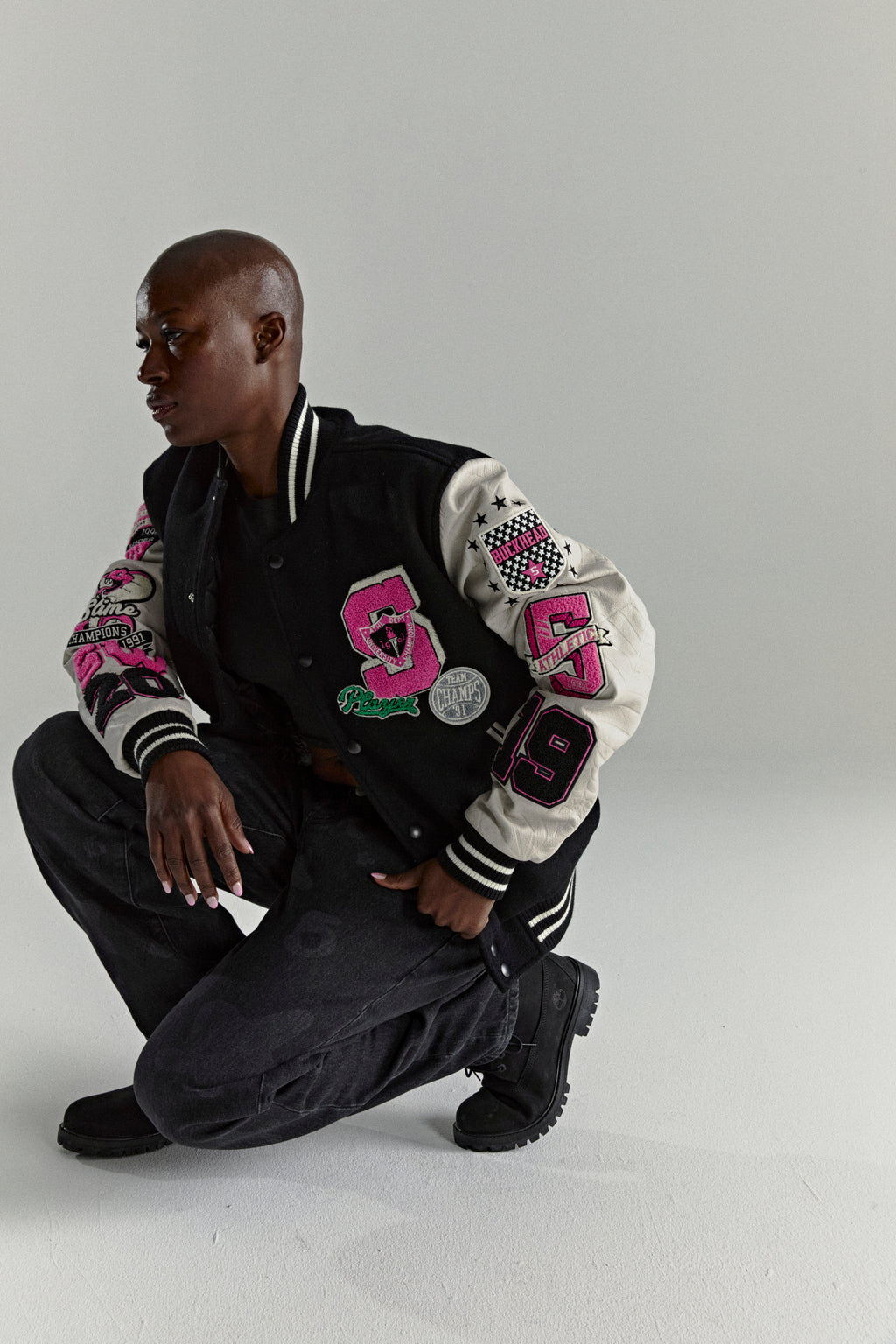 Black wool varsity jacket with contrasting leather sleeves, pink patches, and striped ribbed trim.