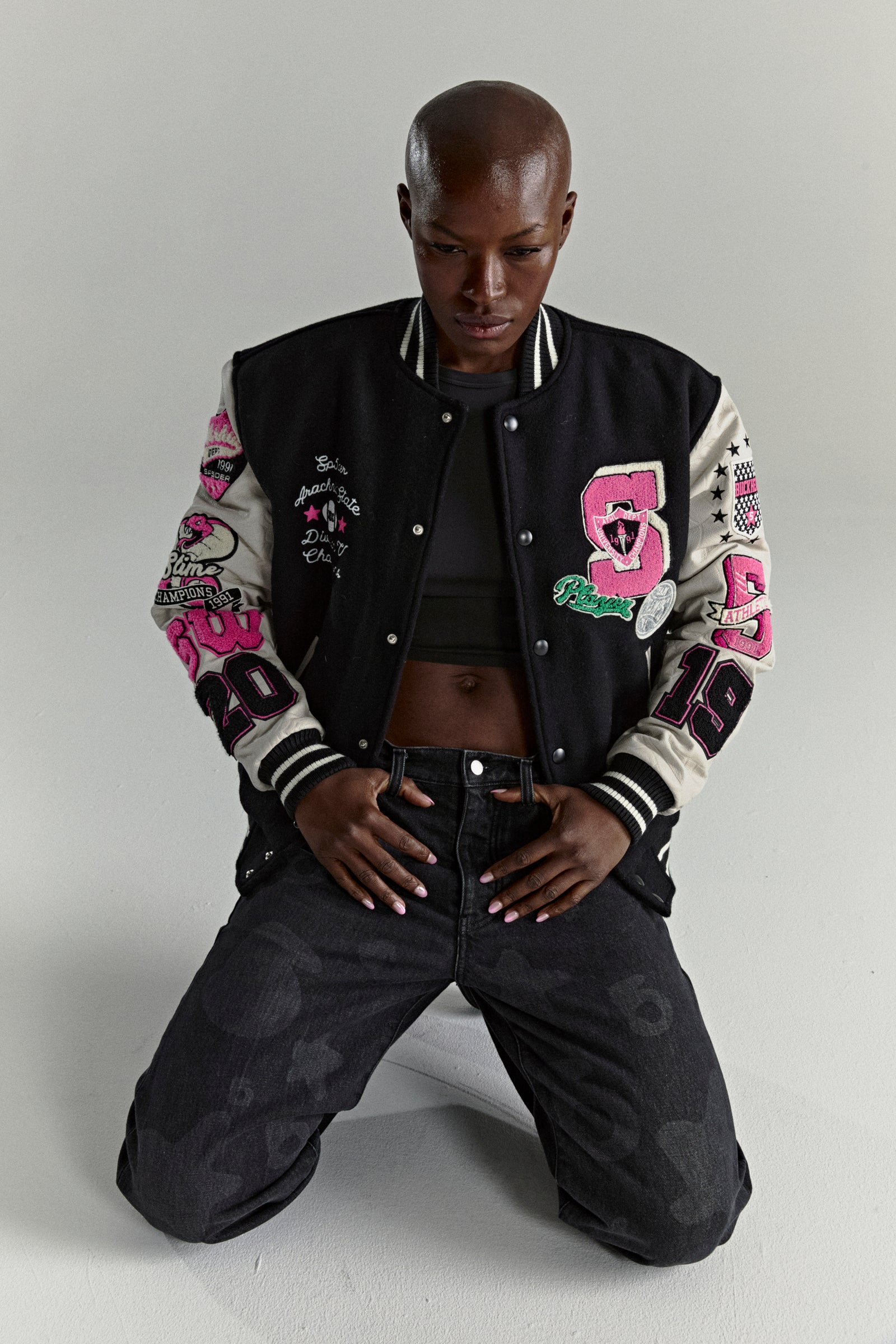 Black wool varsity jacket with contrasting leather sleeves, pink patches, and striped ribbed trim.