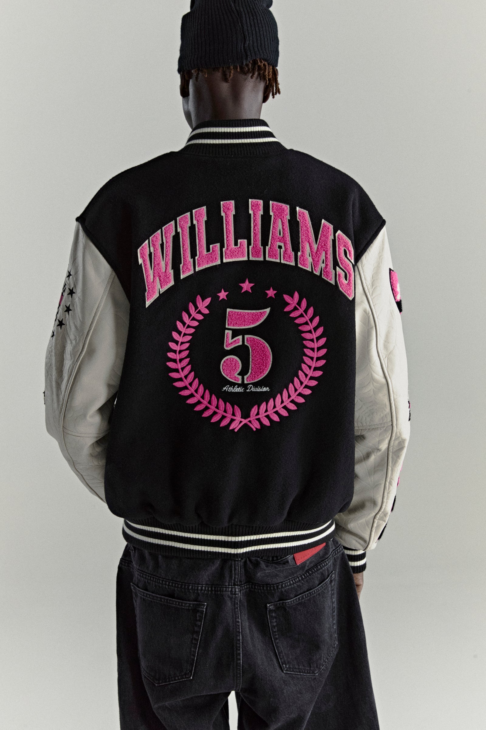 Black wool varsity jacket with cream leather sleeves, pink "WILLIAMS 5" embroidery, and star appliqués.