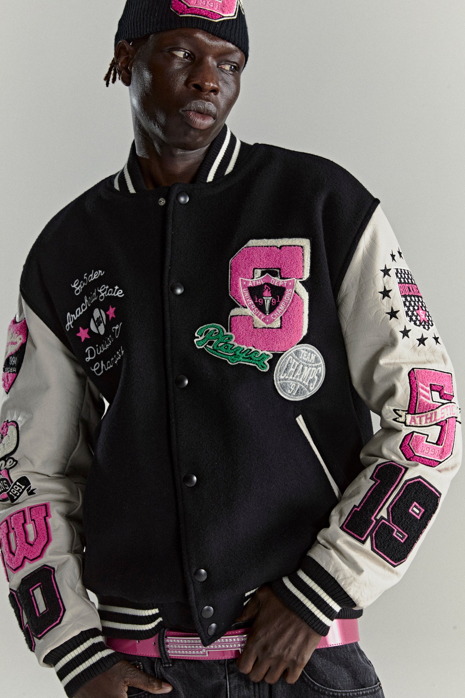 Black wool varsity jacket with cream leather sleeves, pink patches, and striped trim.