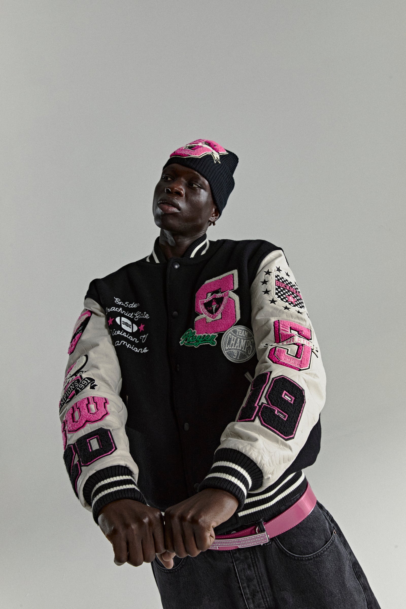 Black wool varsity jacket with white leather sleeves, pink patches, and striped ribbed trim.