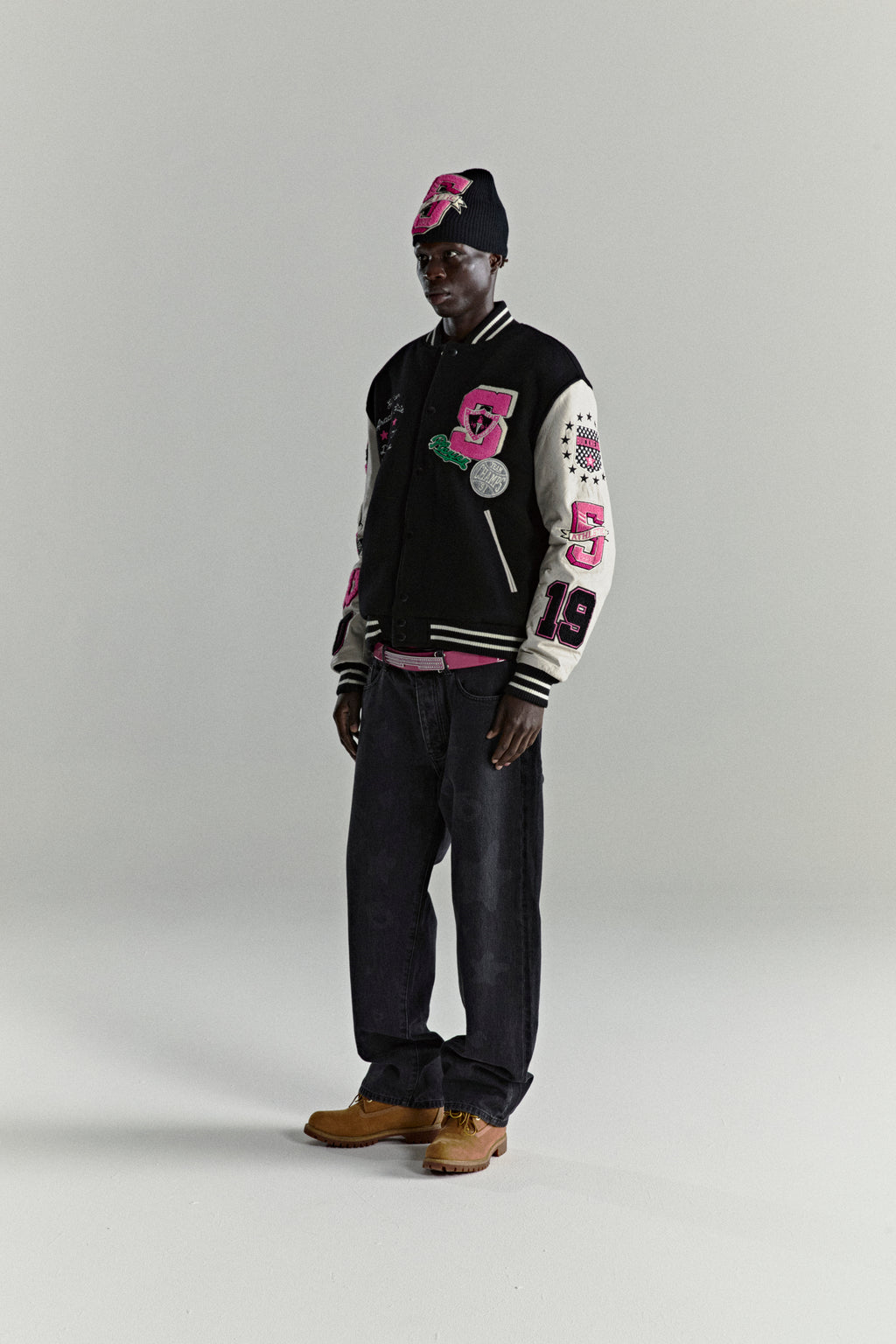 Black wool varsity jacket with cream leather sleeves, pink patches, and a matching beanie.