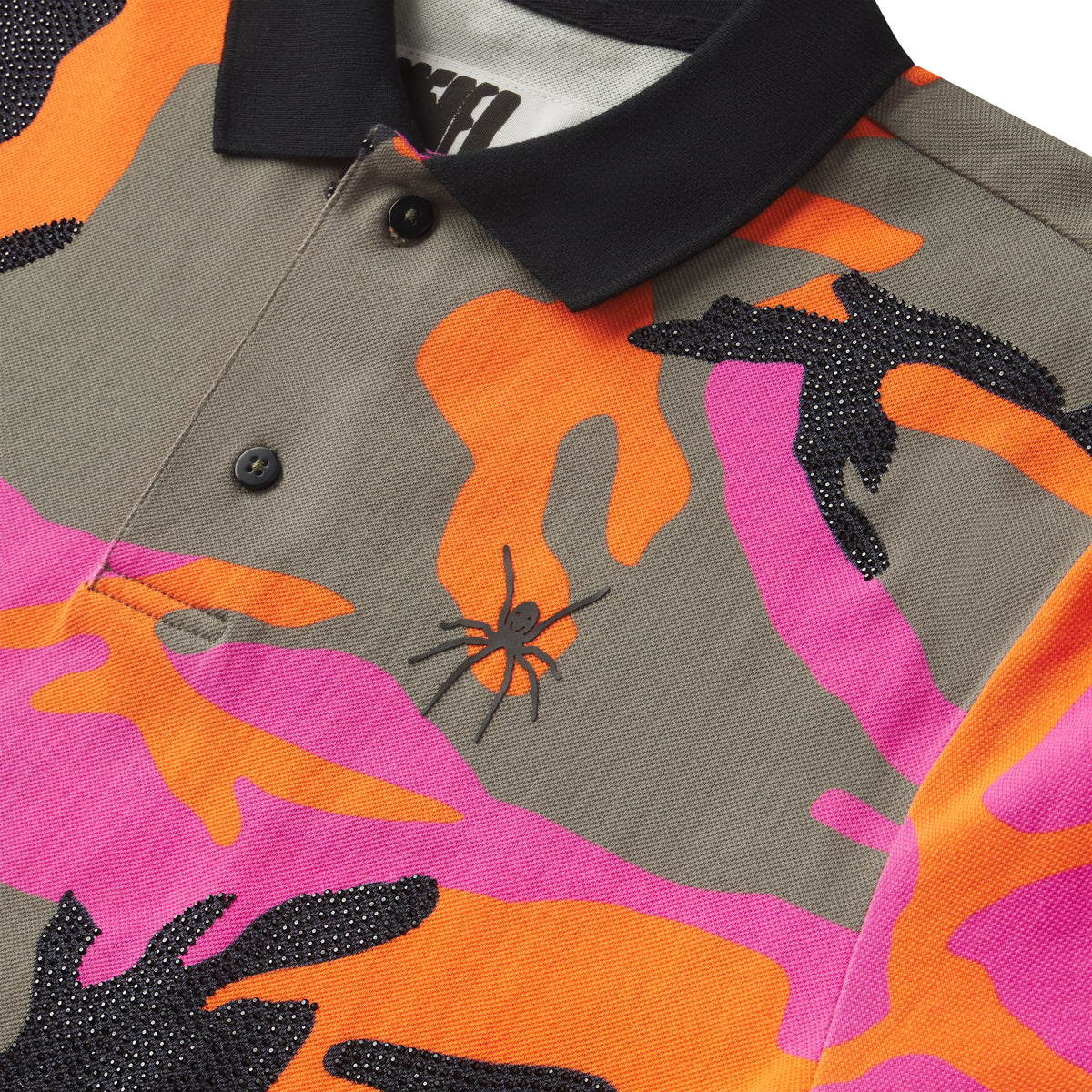 Cotton polo with pink, orange, and grey camo graphic print, black rhinestone embellishments, and a spider logo on the chest.