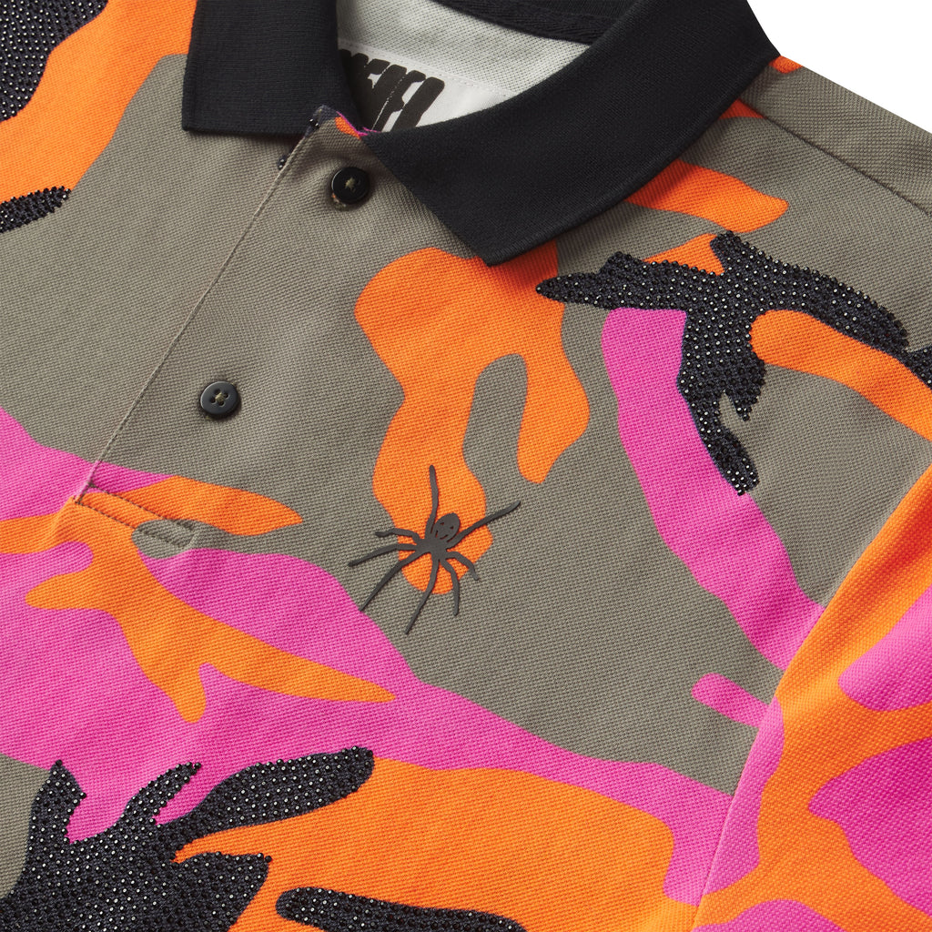 Cotton polo with pink, orange, and grey camo graphic print, black rhinestone embellishments, and a spider logo on the chest.