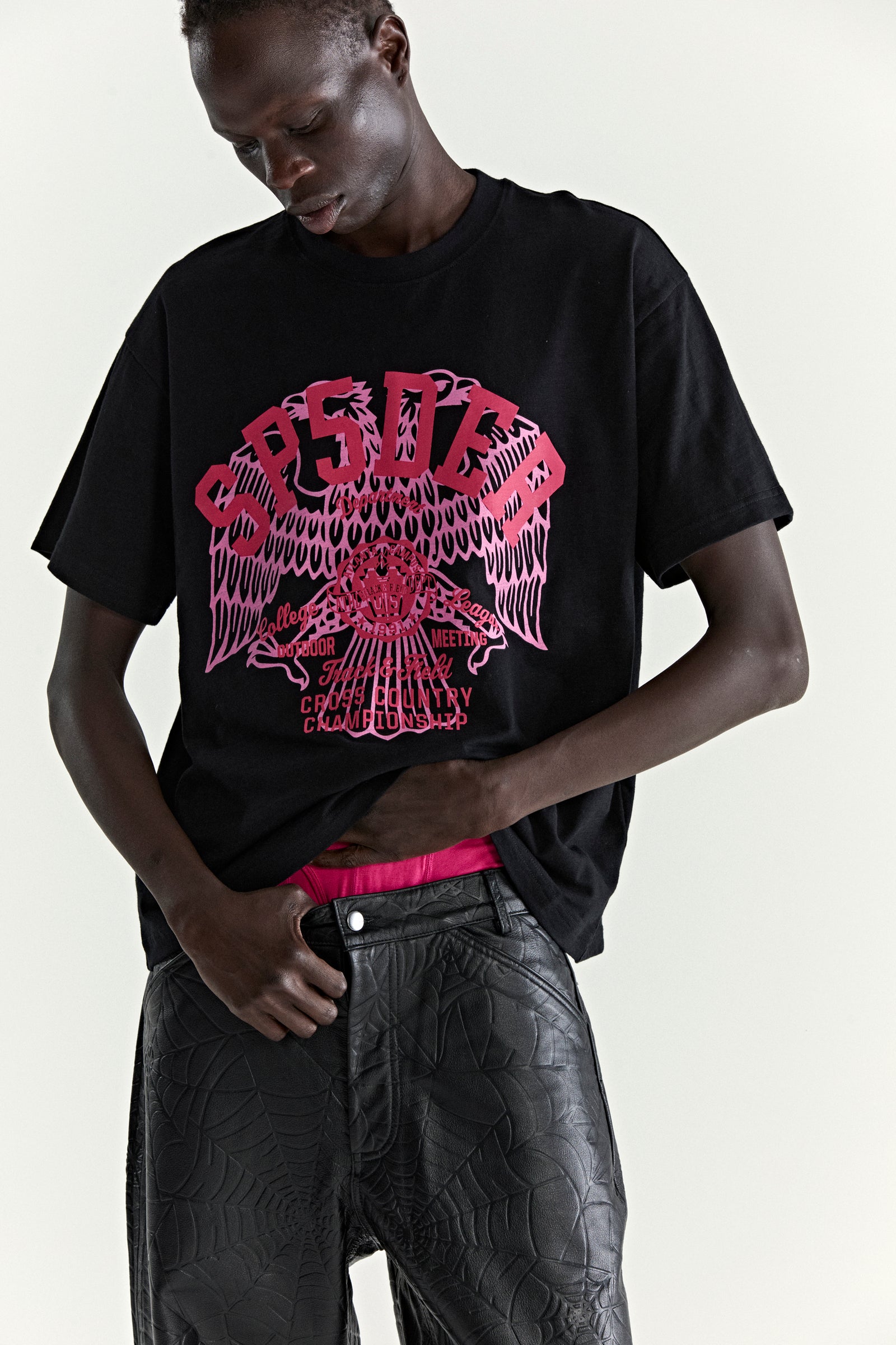 Black slub jersey tee with a large pink graphic print of an eagle and text, worn by a man.