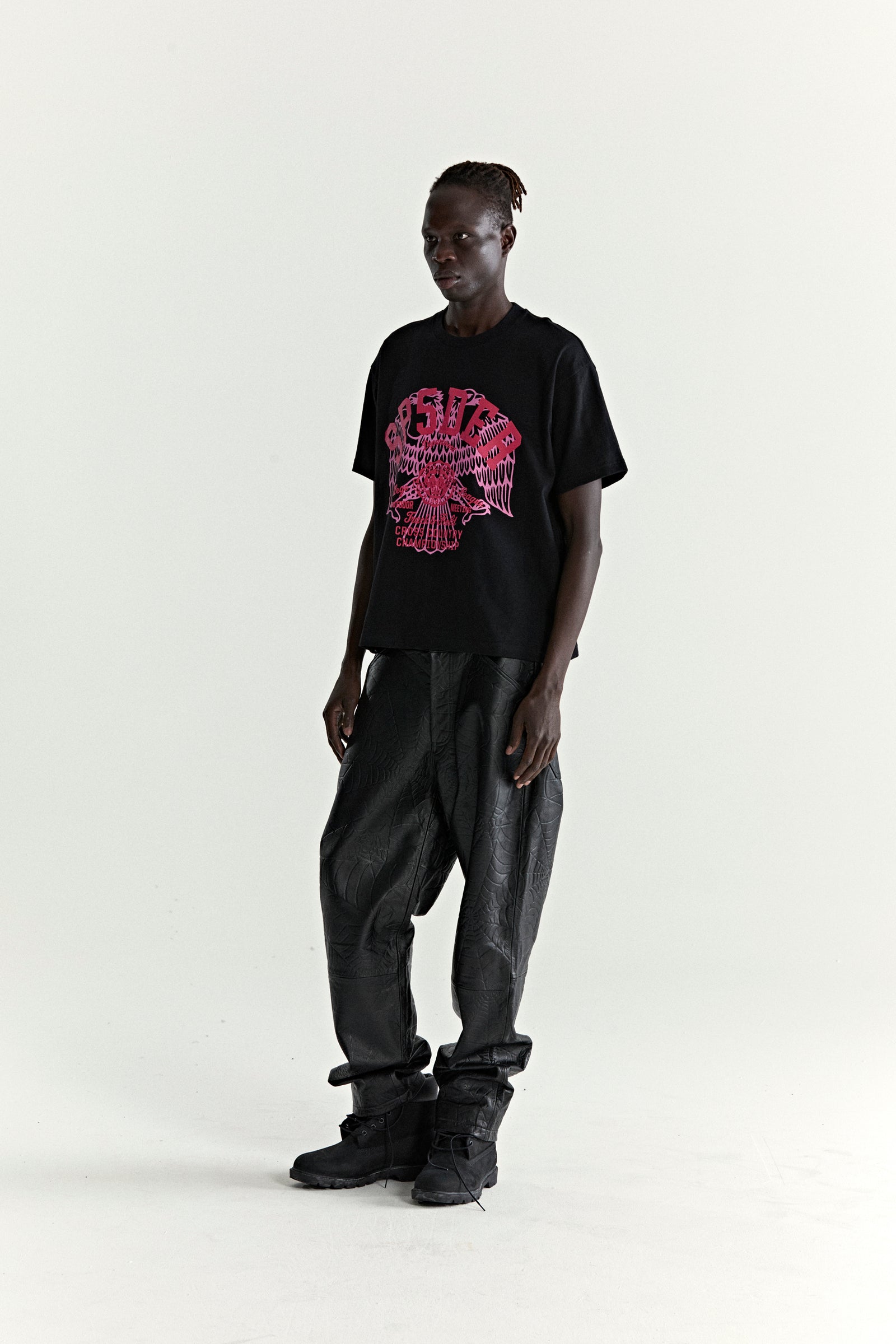 Black slub jersey tee with a red graphic eagle print, paired with black textured pants and boots.