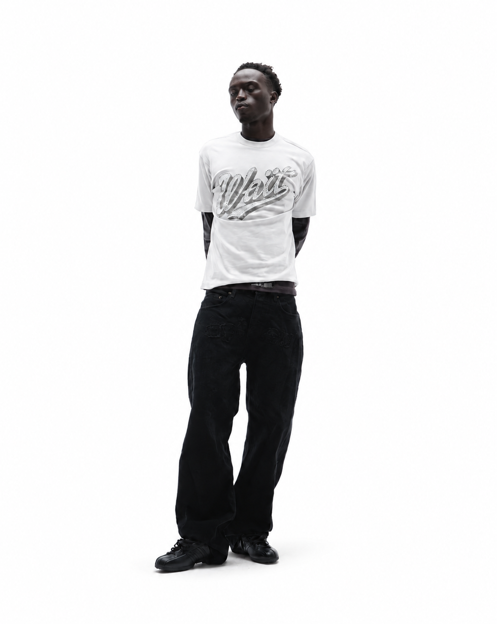 Model wearing a white graphic t-shirt with metallic lettering and loose-fitting black jeans against a white background.