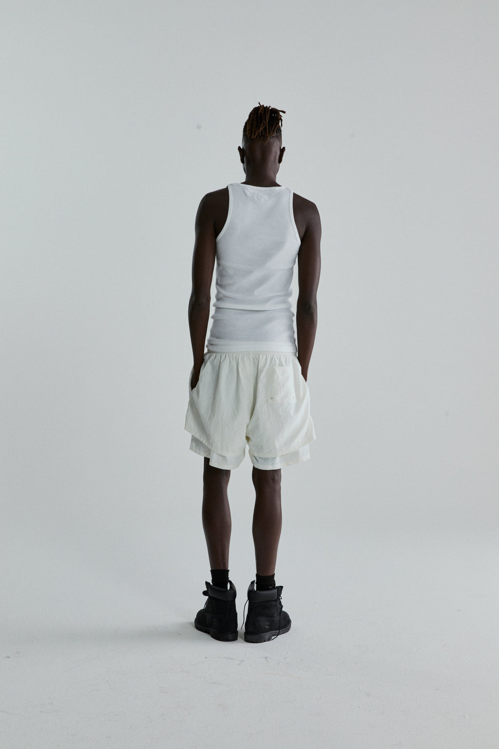 Rear view of a person wearing white OG WEB DOUBLE LAYER SHORT with a high-low design and a white tank top.