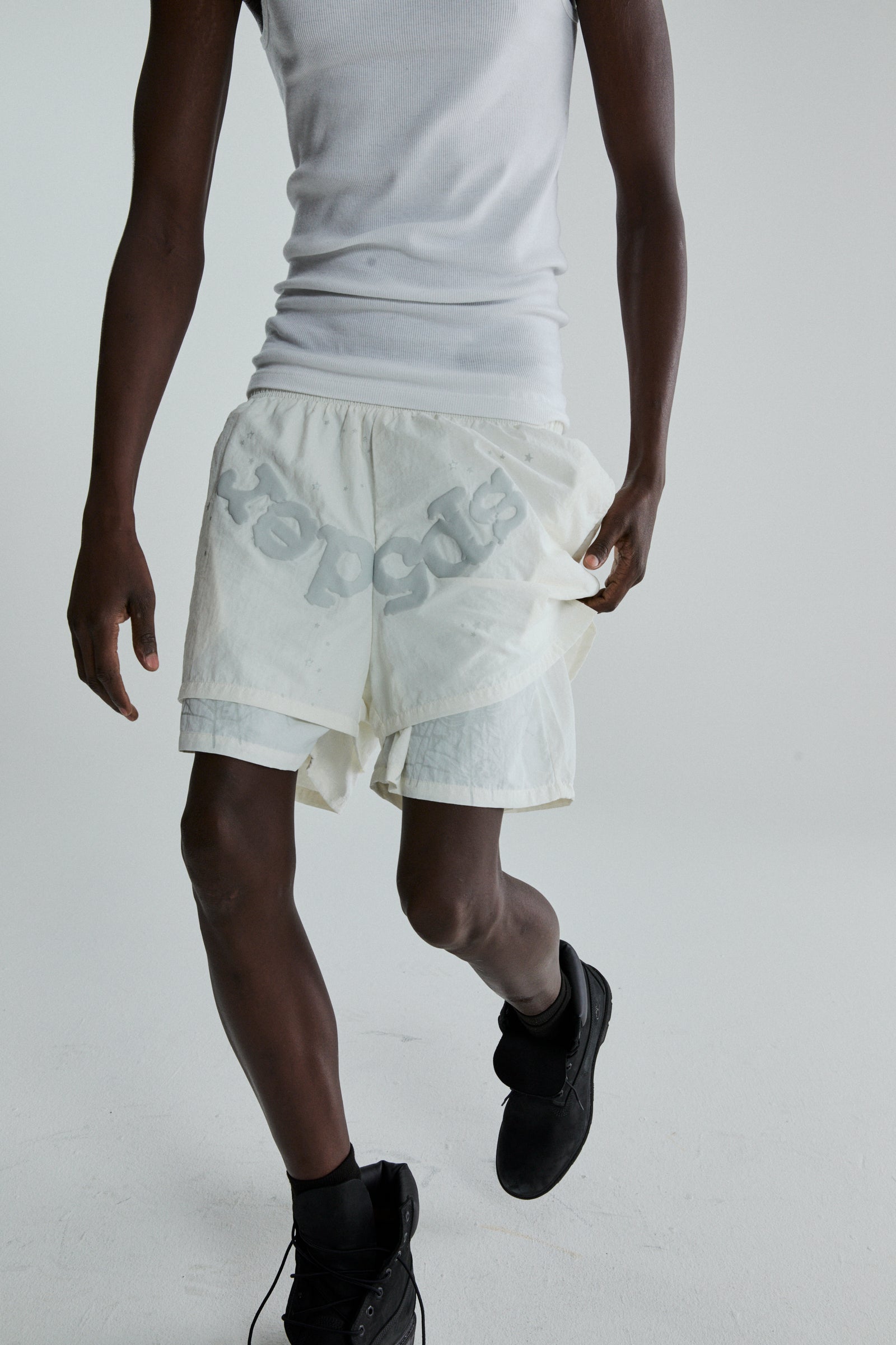 Model wearing OG WEB Double Layer Short in white water repellent nylon with "sp5der" text and star print.