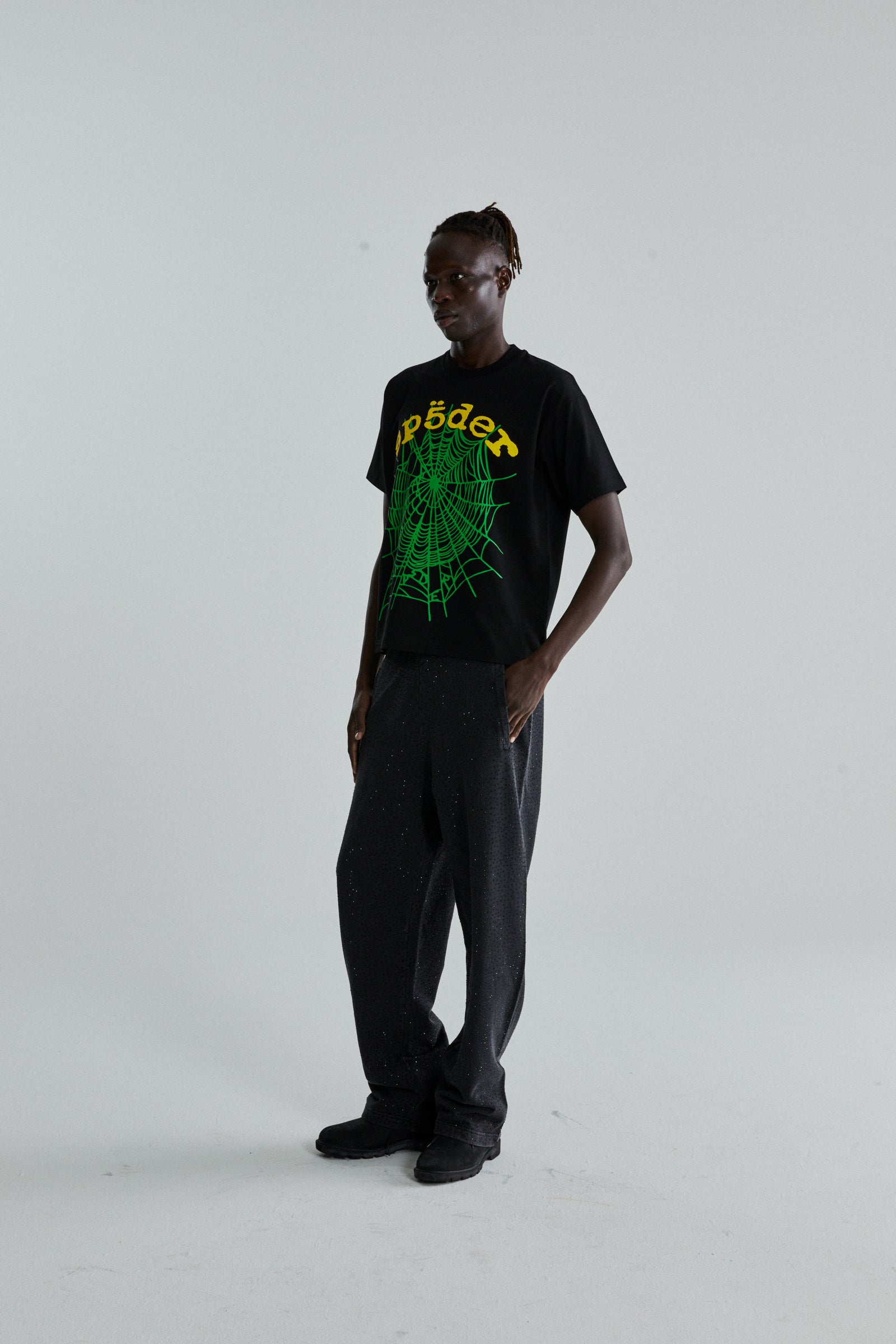 Man in black OG WEB V2 TEE with green spiderweb print, black pants, and shoes.