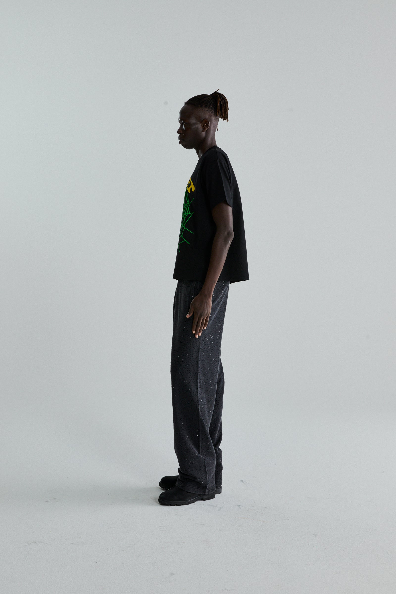 Model in black OG WEB V2 TEE with green and yellow puff/discharge print, paired with dark grey pants.