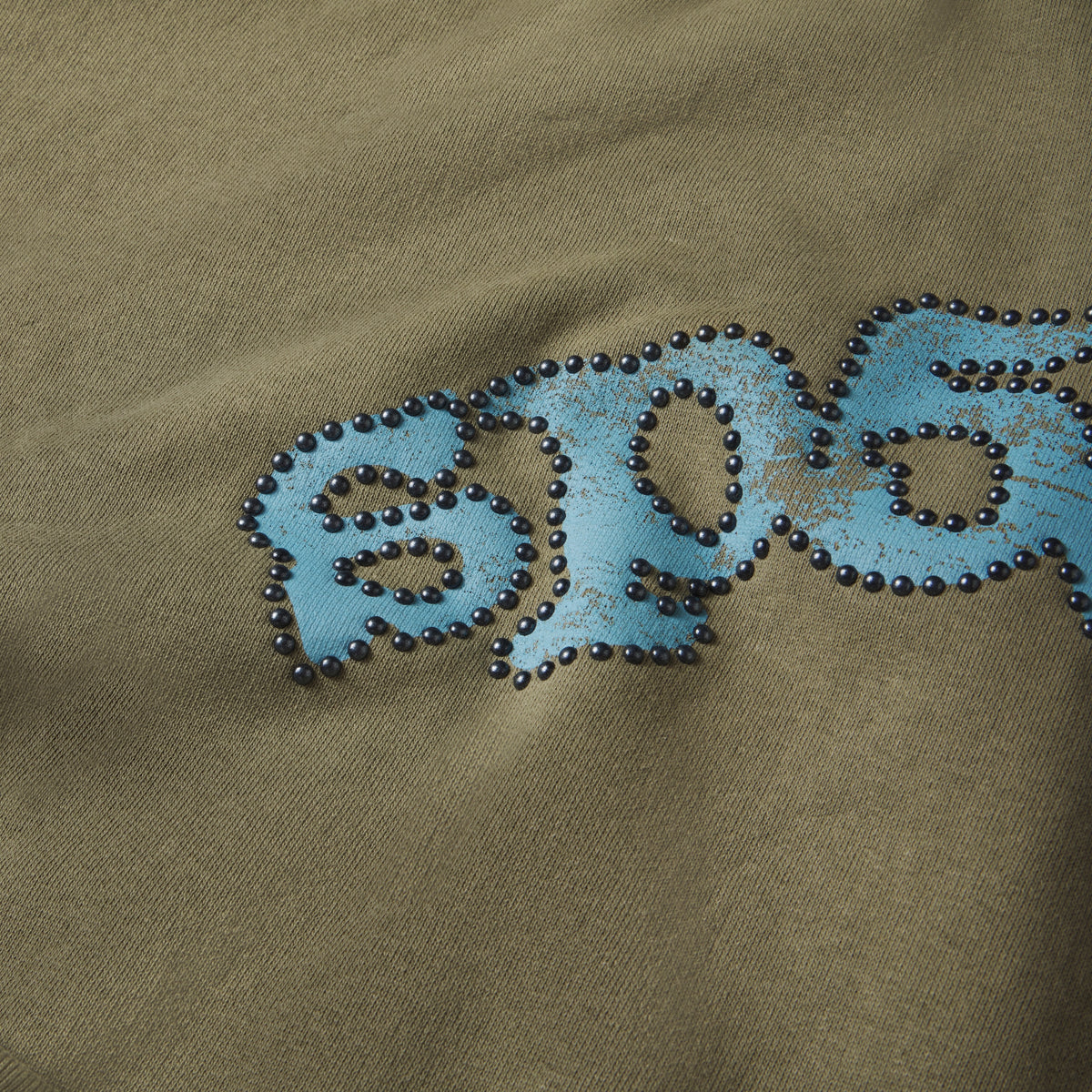 Olive green cotton fleece hoodie featuring a distressed blue graphic logo outlined with metallic studs.