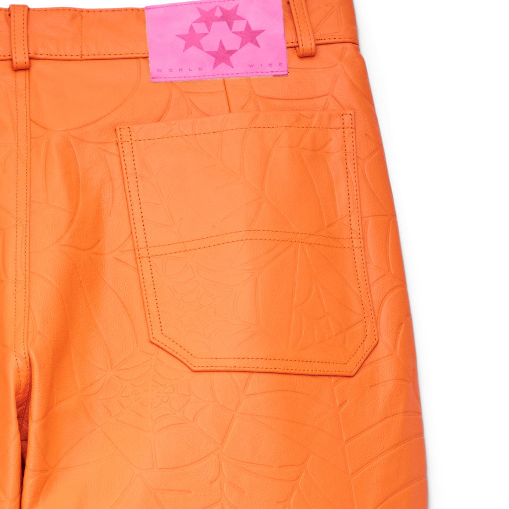 Orange cowskin leather pants with debossed web design, back pocket, and pink suede logo patch.