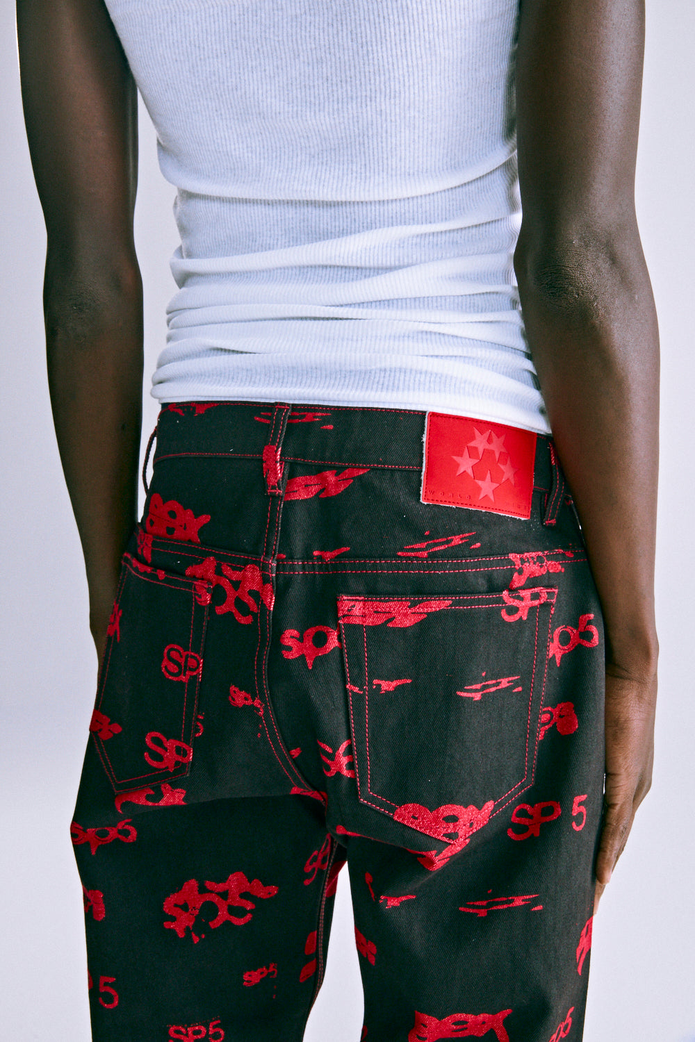 Black denim pants with red all-over print, red contrast stitching, and a red leather SP5DER patch.
