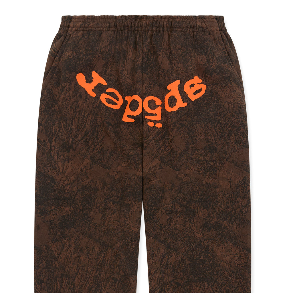 Brown tree camo sweatpants with orange SP5DER text at crotch, elastic waistband, and cuffs.