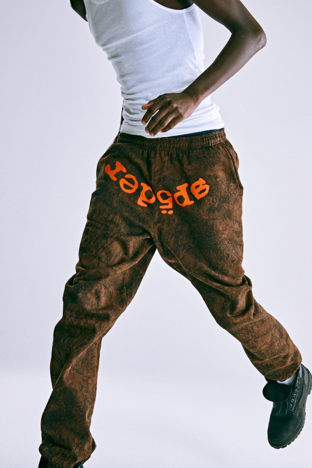 Brown tree camo cotton fleece sweatpants with orange SP5DER text at crotch, drawstring, and elasticized cuffs.