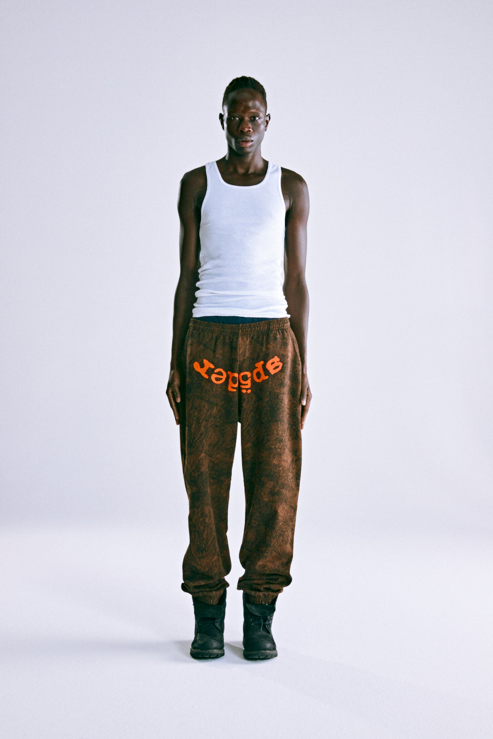 Brown tree camo sweatpants with orange SP5DER text, elasticized waist and cuffs, worn by a model.