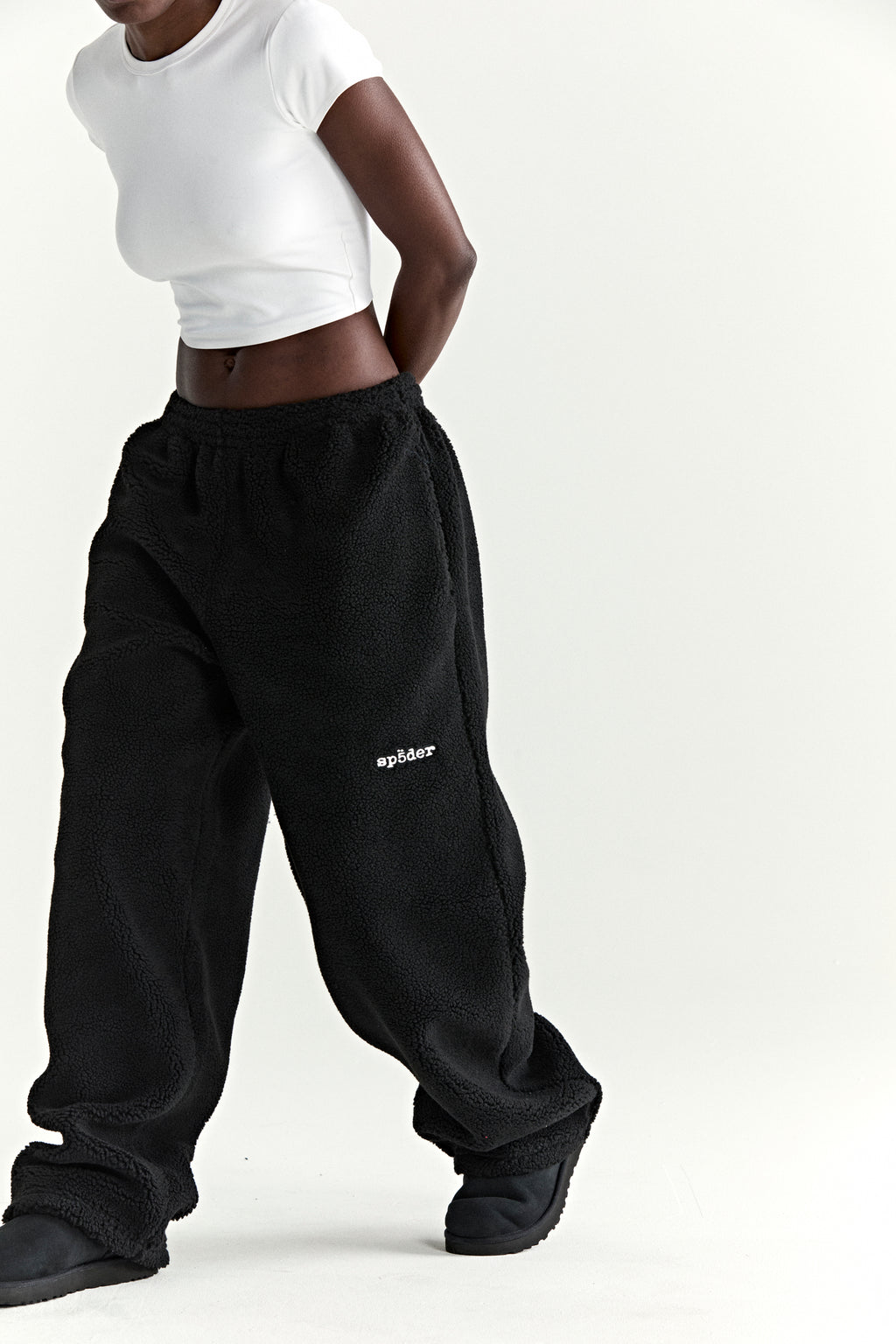 Black teddy fleece pants with white "sp5der" logo, drawstring elastic waistband, and straight leg fit.