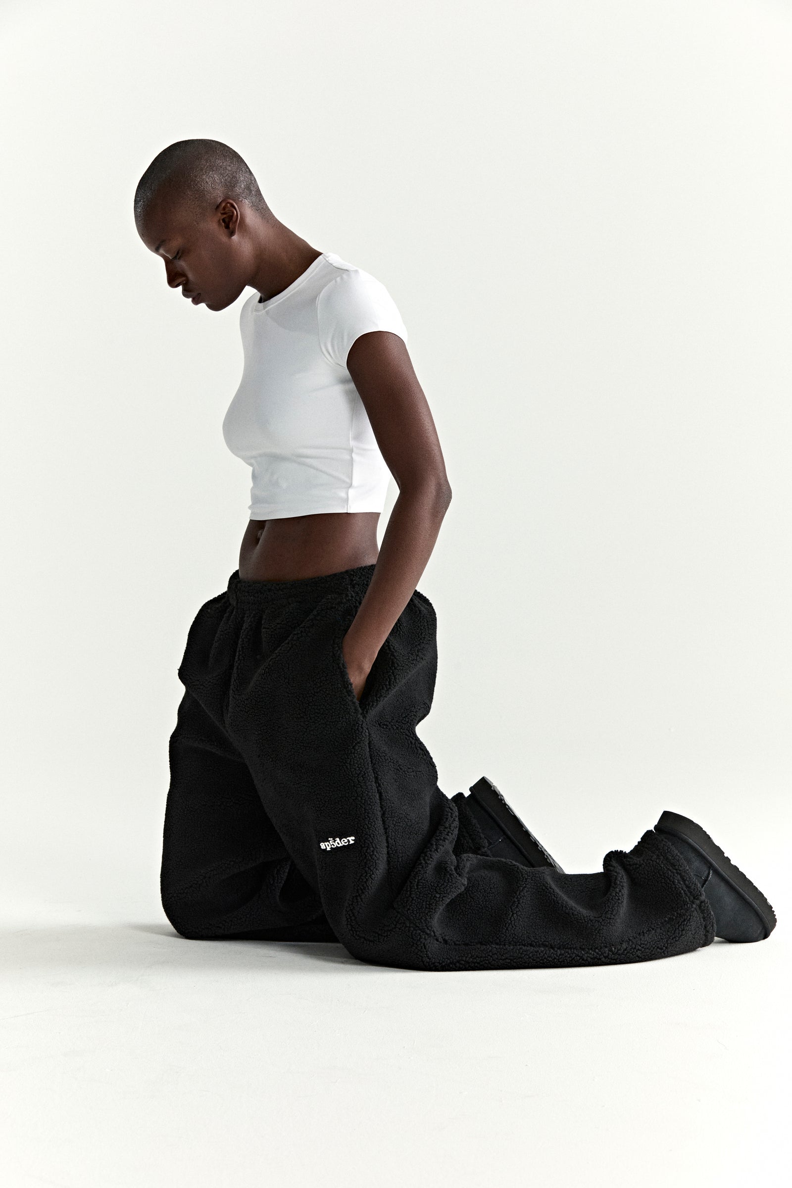 Black teddy fleece pants with white rubberized logo patch, worn by a person kneeling.