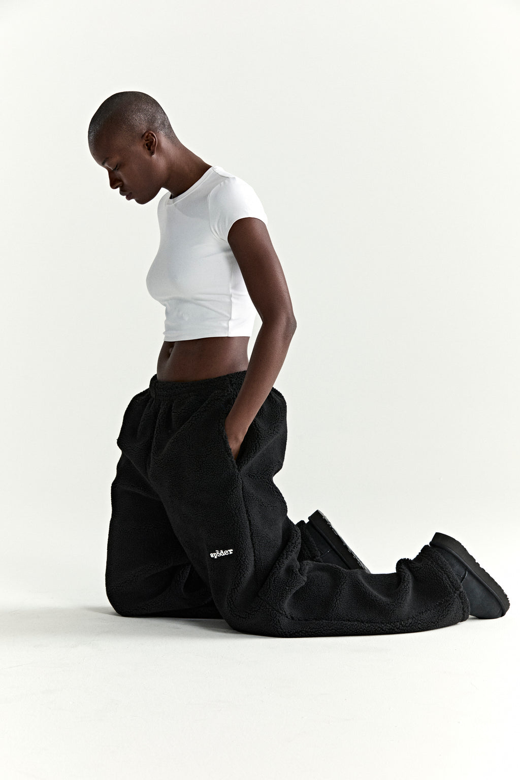 Black teddy fleece pants with white rubberized logo patch, worn by a person kneeling.