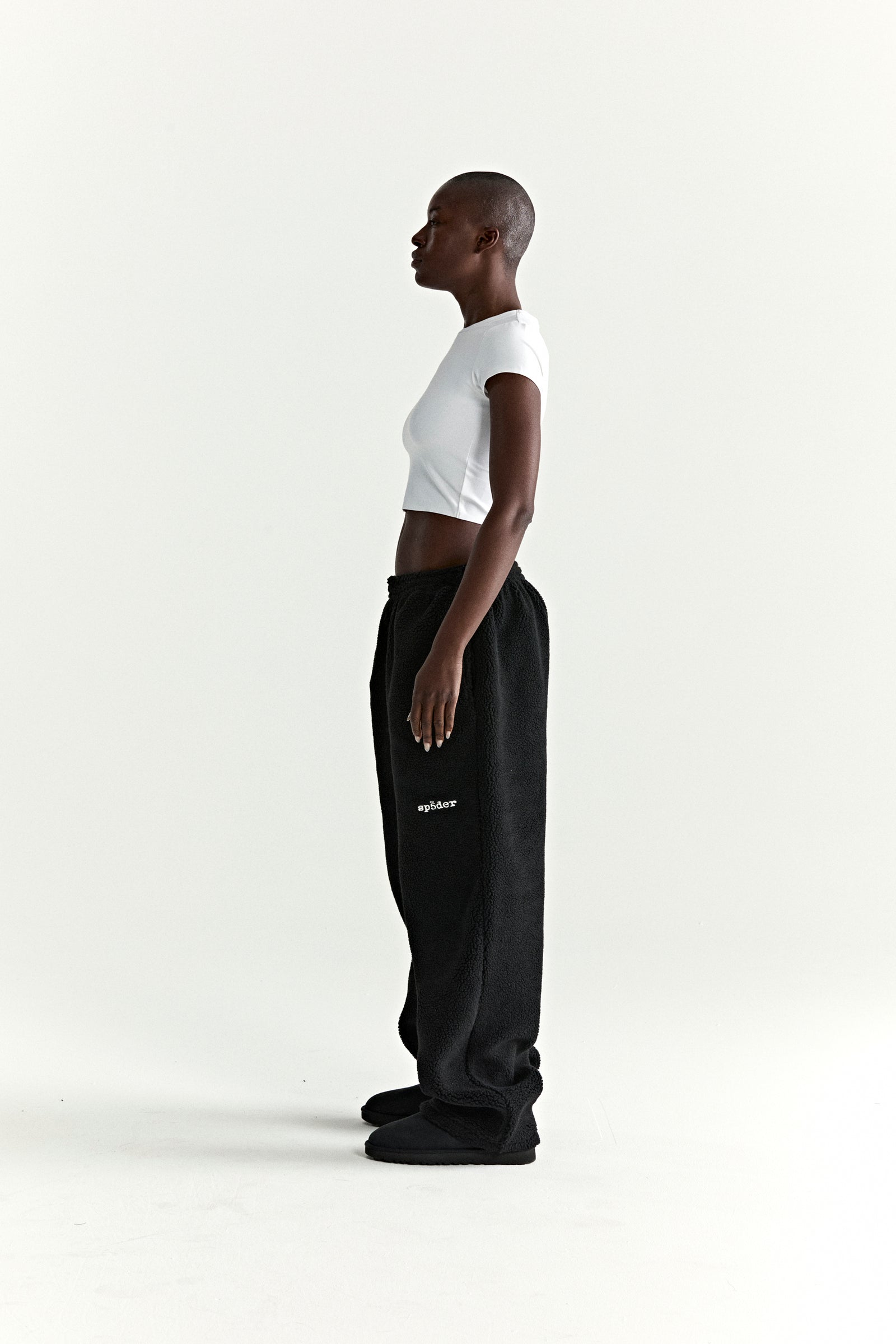 Black teddy fleece pant with rubberized logo patch on leg, worn by a model.