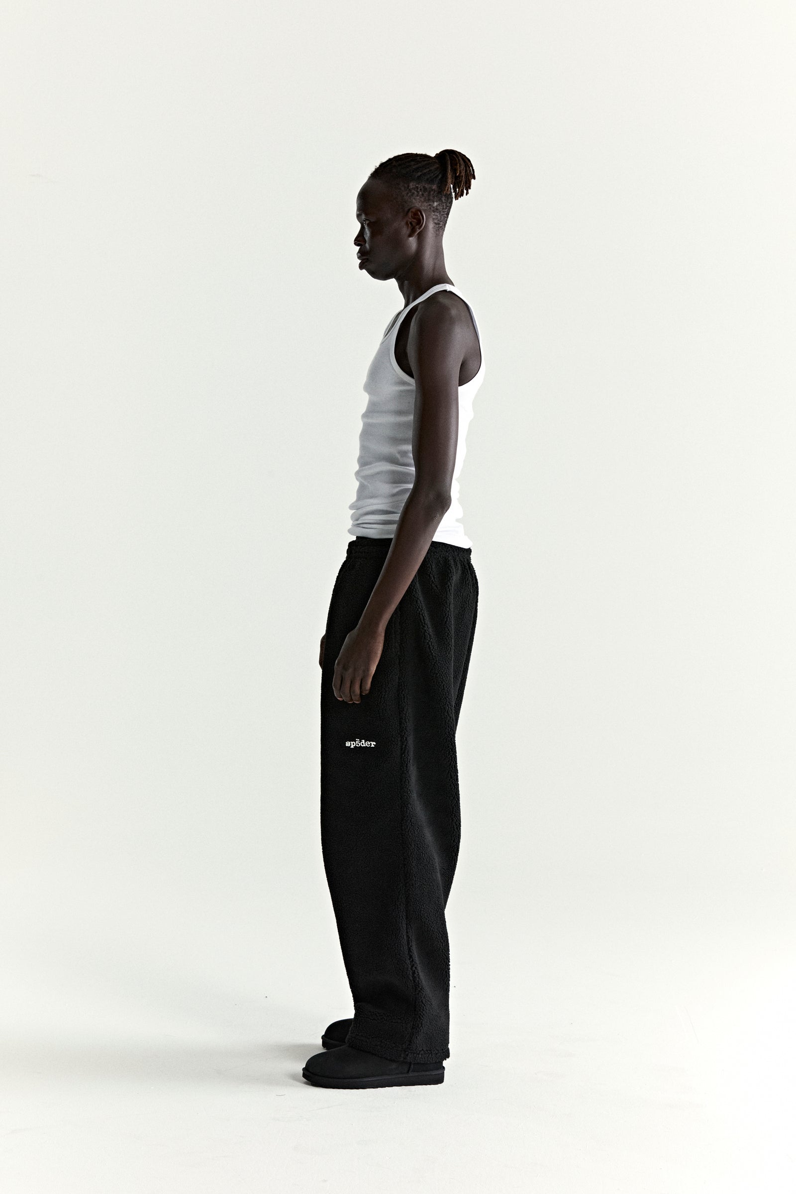 Man in black teddy fleece pants with white logo patch and straight leg fit.