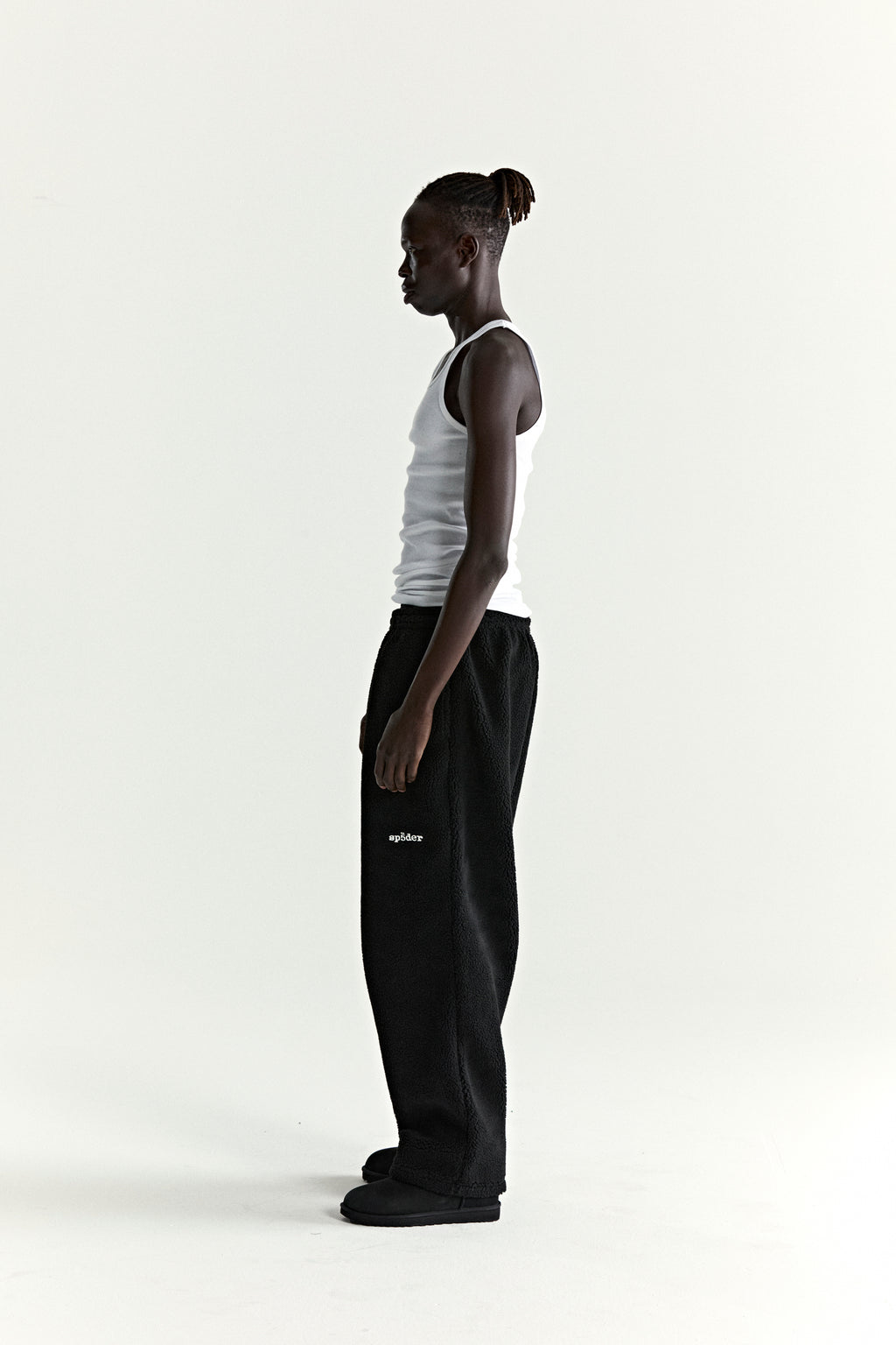 Man in black teddy fleece pants with white logo patch and straight leg fit.