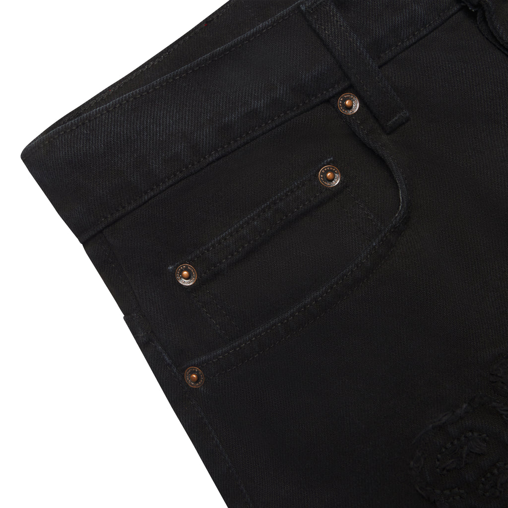 Close-up of black distressed denim jeans with custom branded hardware and frayed embroidered logo.