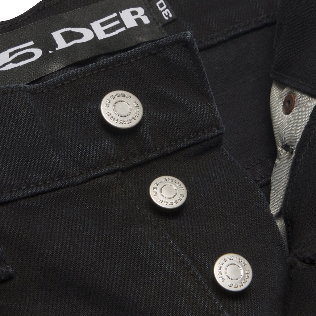 Close-up of black 13oz denim with branded silver shank buttons and "SP5DER" logo tag.