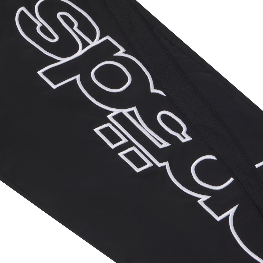 Black nylon track pant featuring white embroidered graphic text and a textured mesh side panel accent.