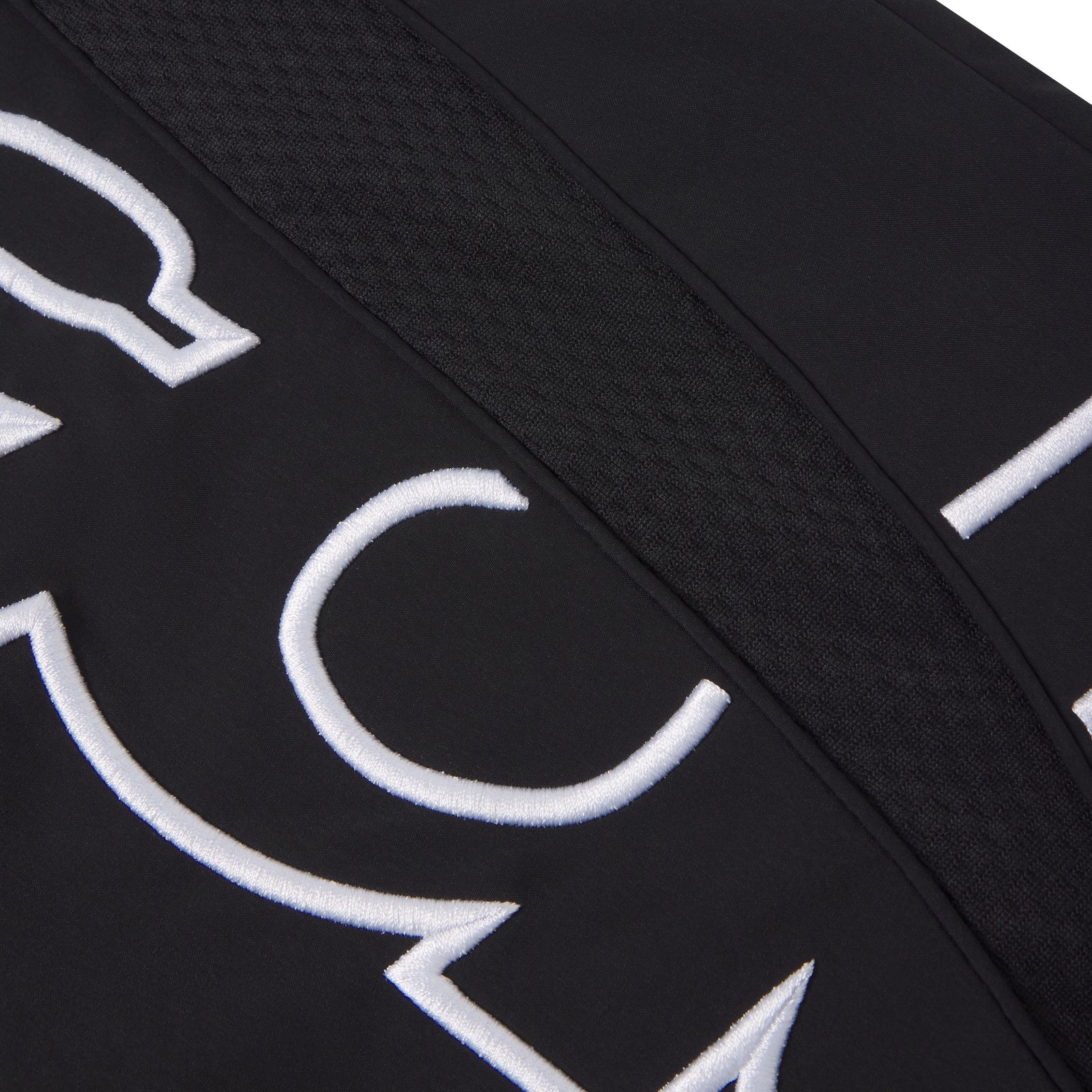 Black nylon track pant featuring white embroidered graphic text and a textured mesh side panel accent.