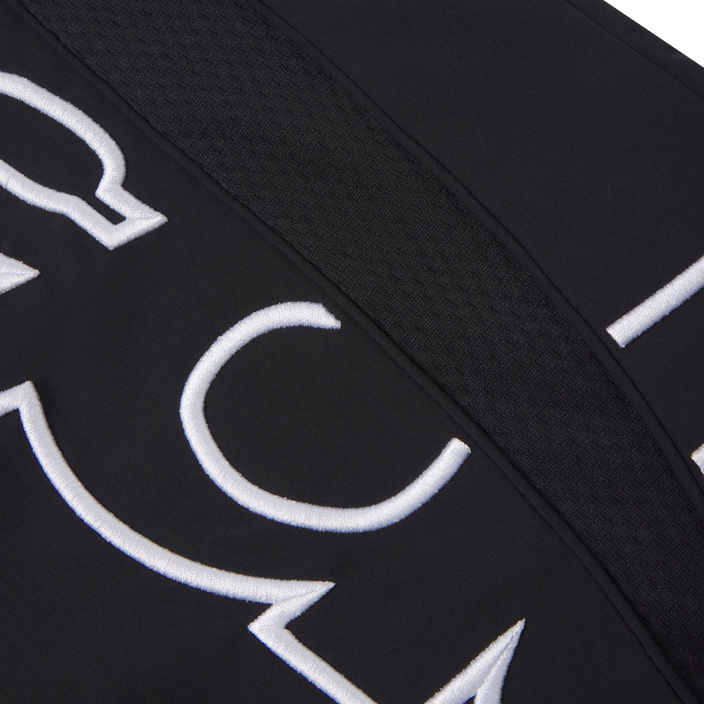 Black nylon track pant featuring white embroidered graphic text and a textured mesh side panel accent.