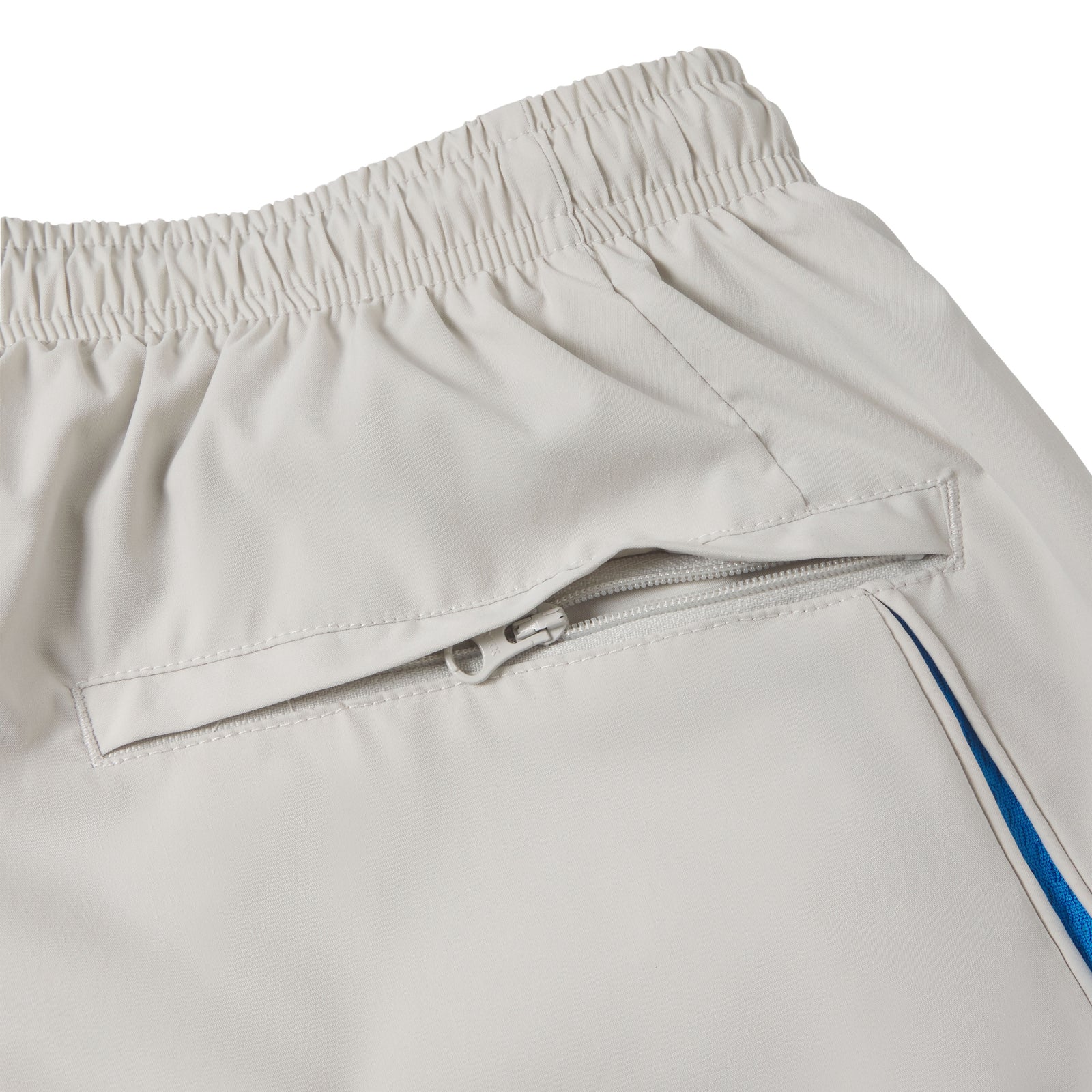 Beige nylon track pant with an elastic waistband, zippered side pocket, and blue contrast side panel detailing.